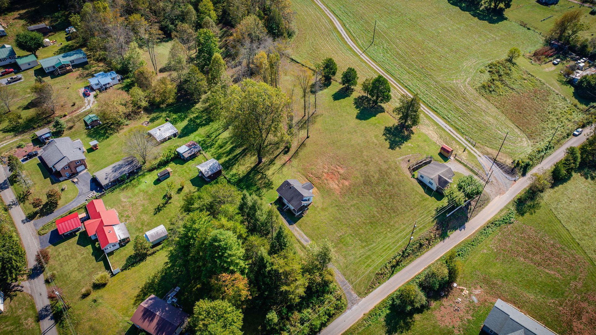 Aerial view of rural homes, trees, fields, and a road in a countryside neighborhood