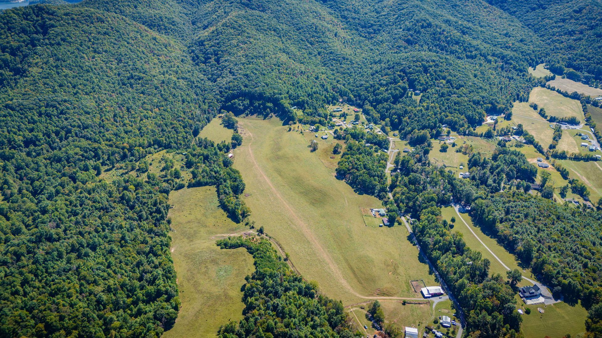 Aerial view of a grassy airstrip surrounded by dense green forest and hills