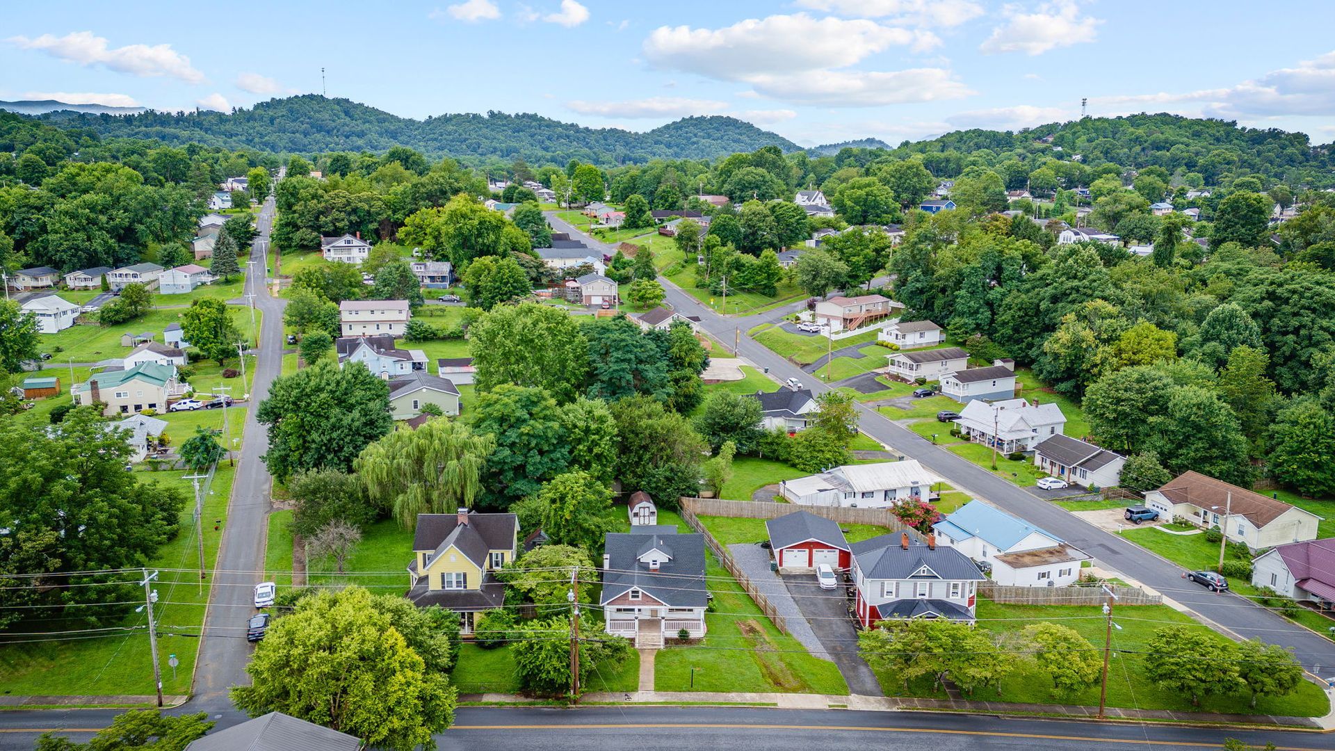 Aerial view of a leafy suburban neighborhood with houses, roads, and hills in the background