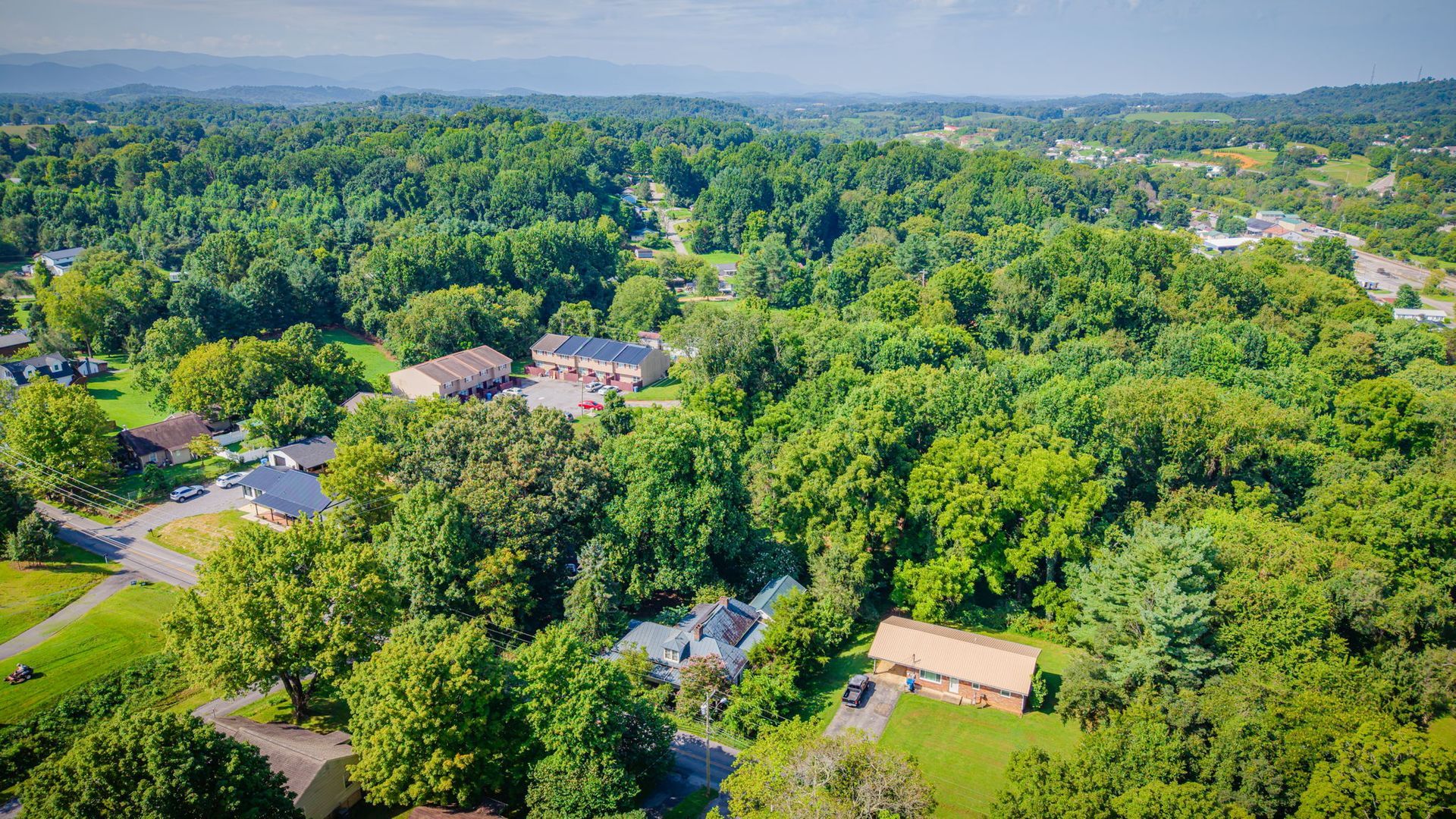 Aerial view of a wooded suburban neighborhood with houses and roads under bright daylight