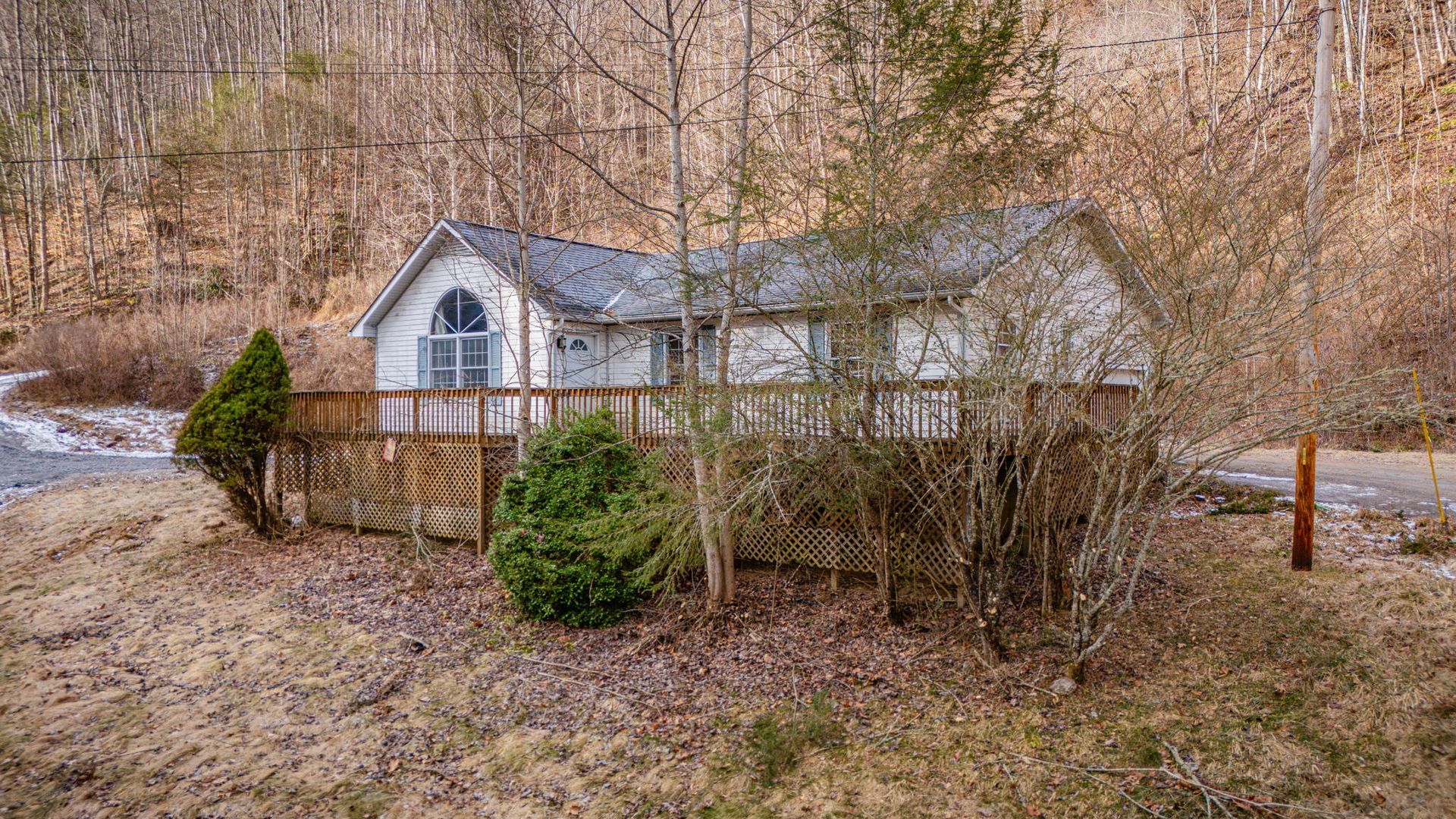 Small white house with a deck in a wooded area, brown landscape, cloudy sky.