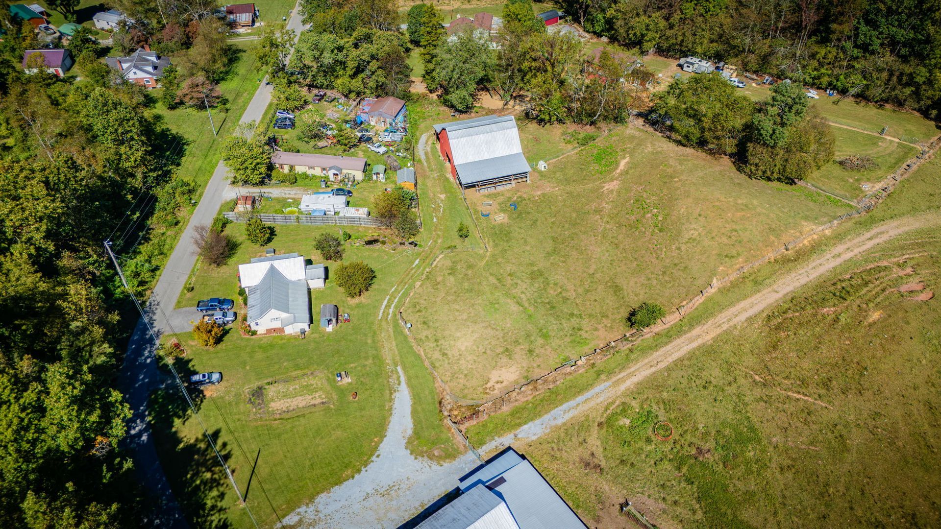 Aerial view of a rural property with a house, barn, driveway, and grassy fields near trees.