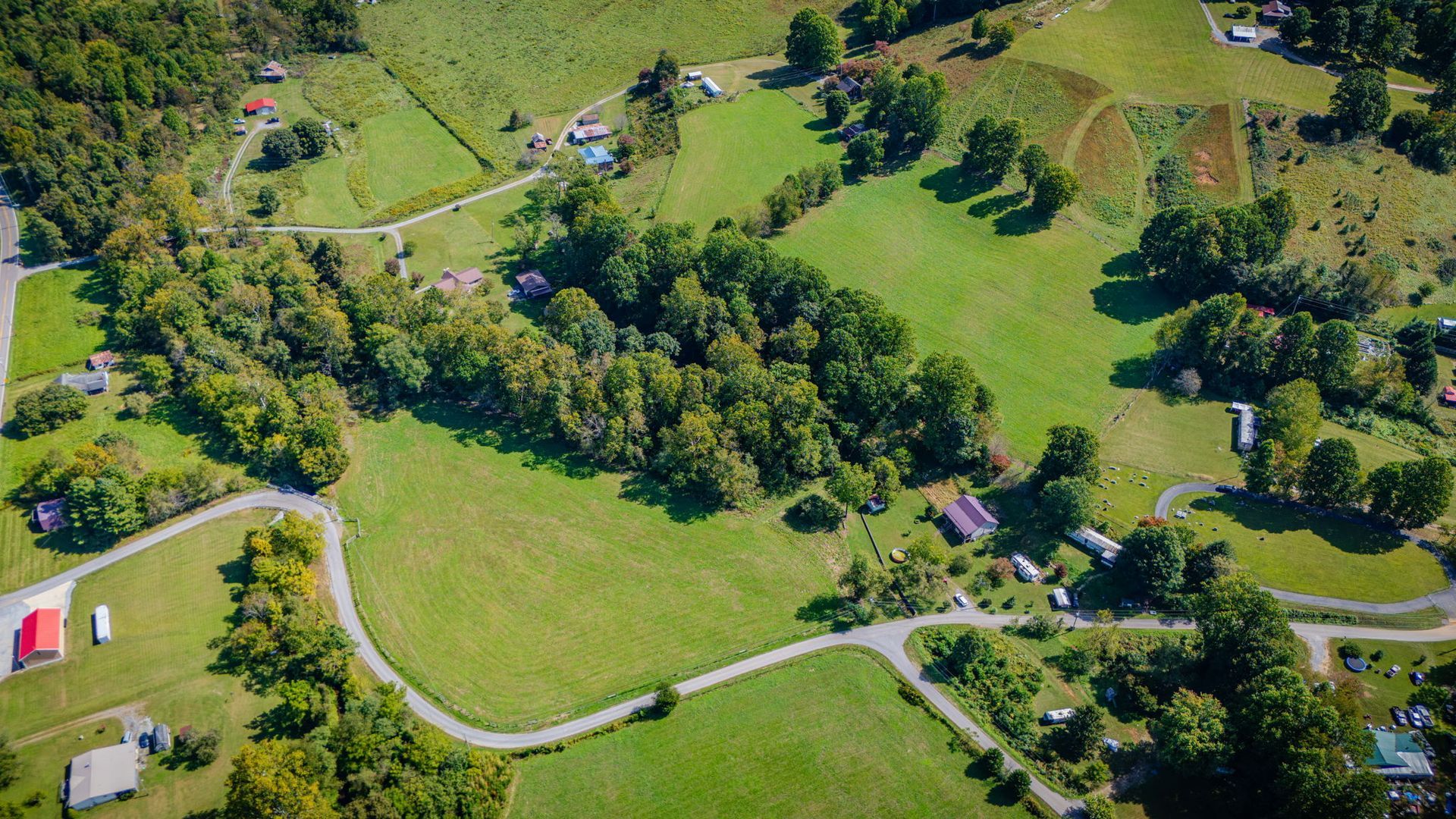 Aerial view of a green park with winding paths, trees, and a small red-roofed building.