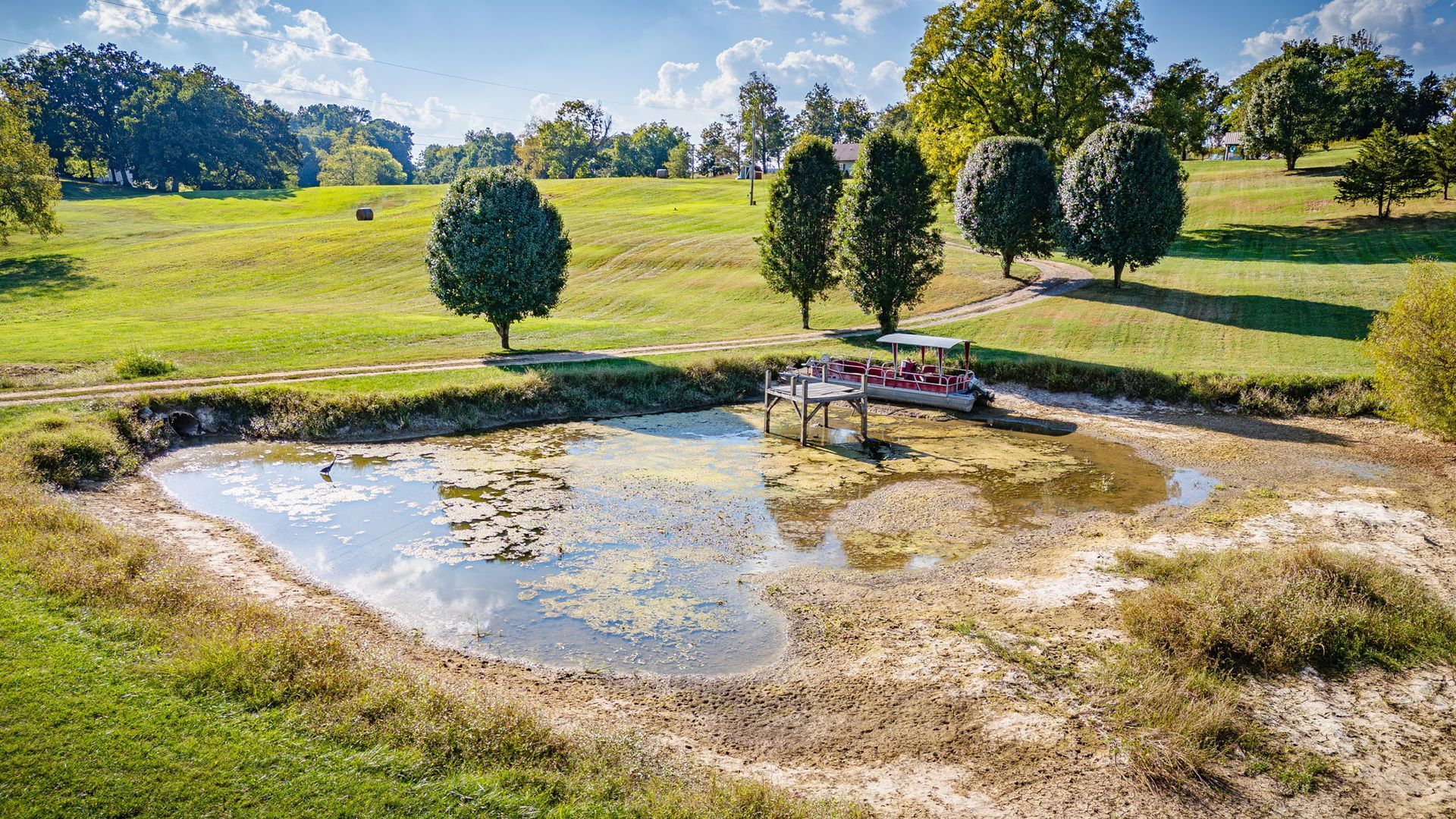 Small pond reflecting sky in a grassy park, with trees and a few benches in the background.