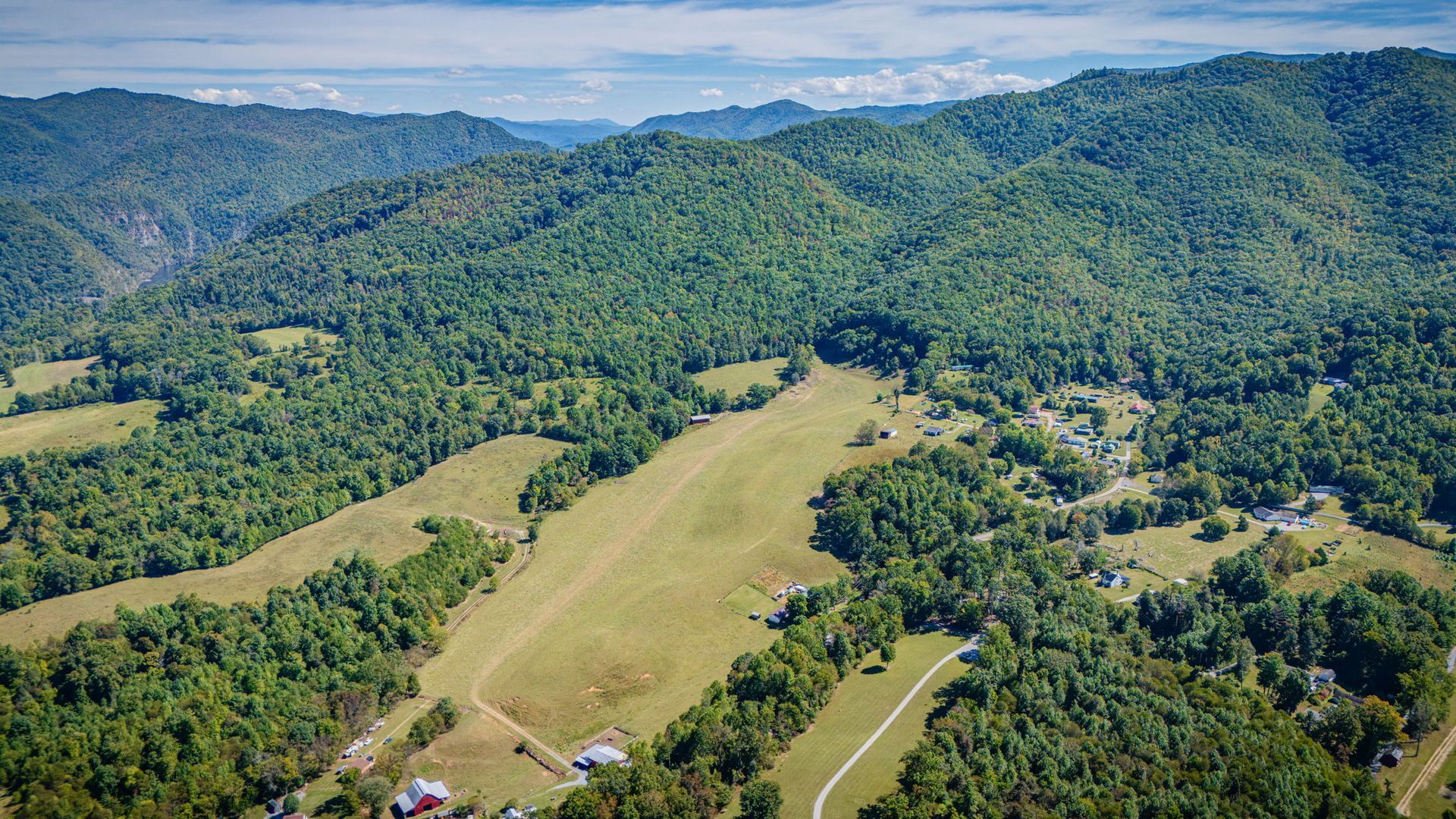 Aerial view of a lush green valley with forested hills, open fields, and a winding road under a clear sky
