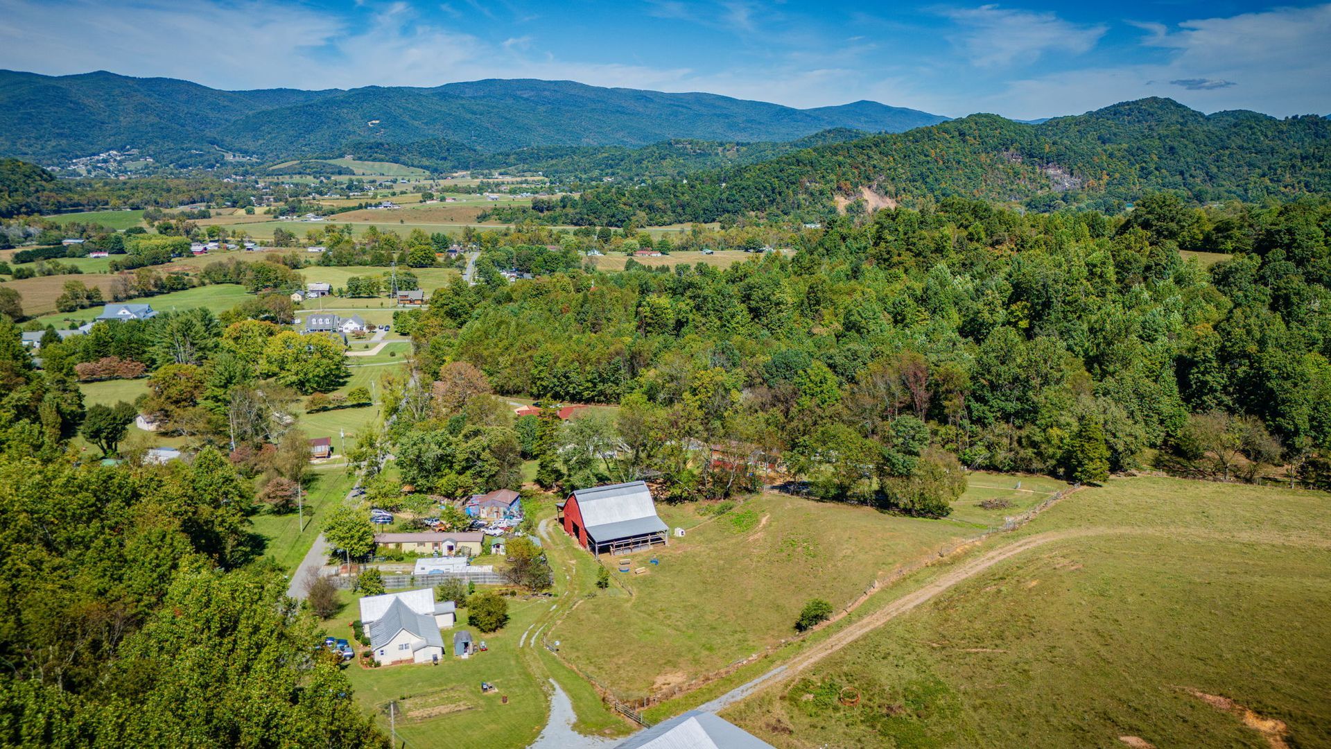 Aerial view of a rural valley with scattered houses, green fields, and forested hills under a clear sky