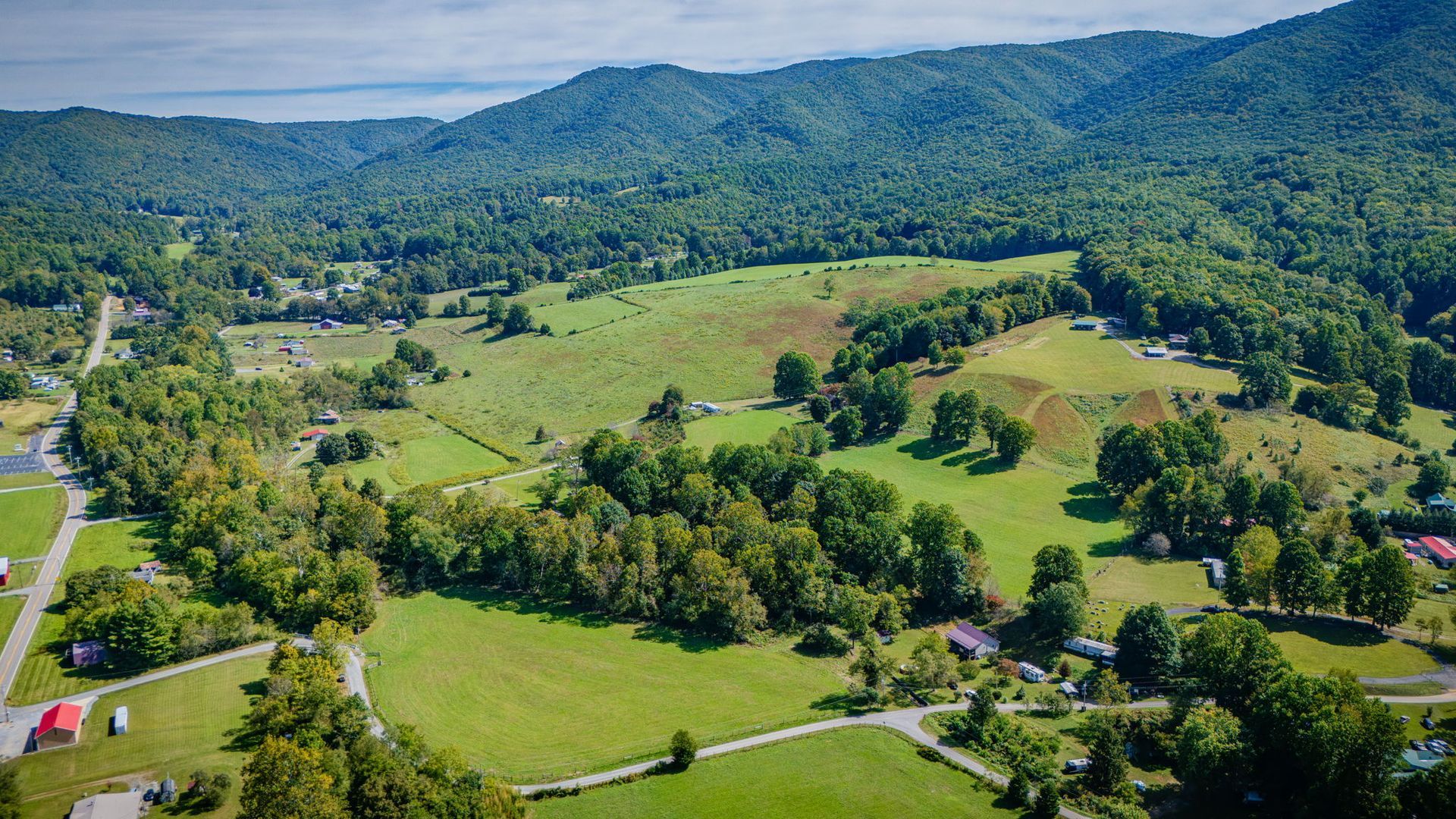 Aerial view of a lush green valley with fields, trees, roads, and forested hills under a clear sky
