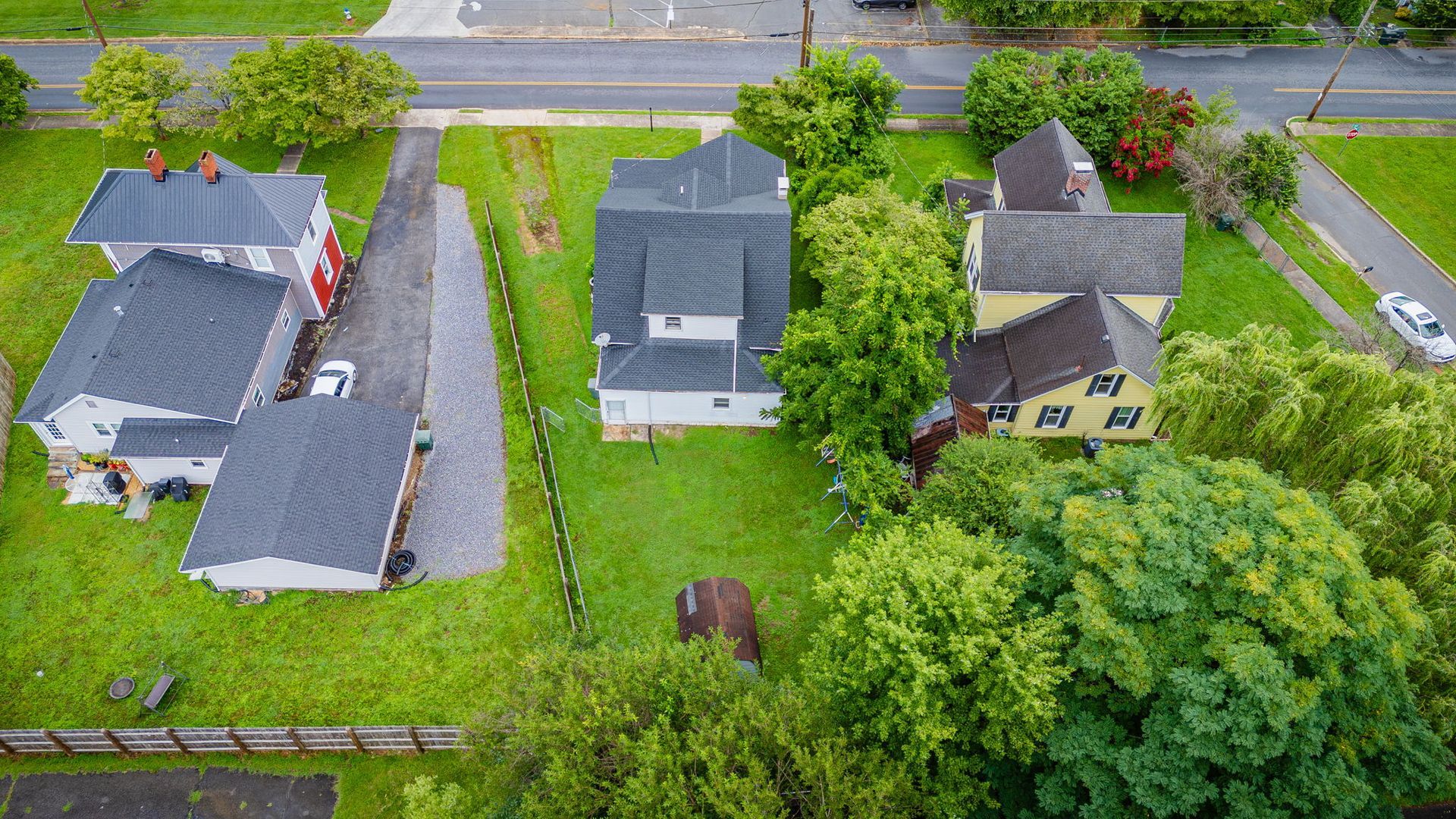 Aerial view of several houses with green lawns and trees beside a road.