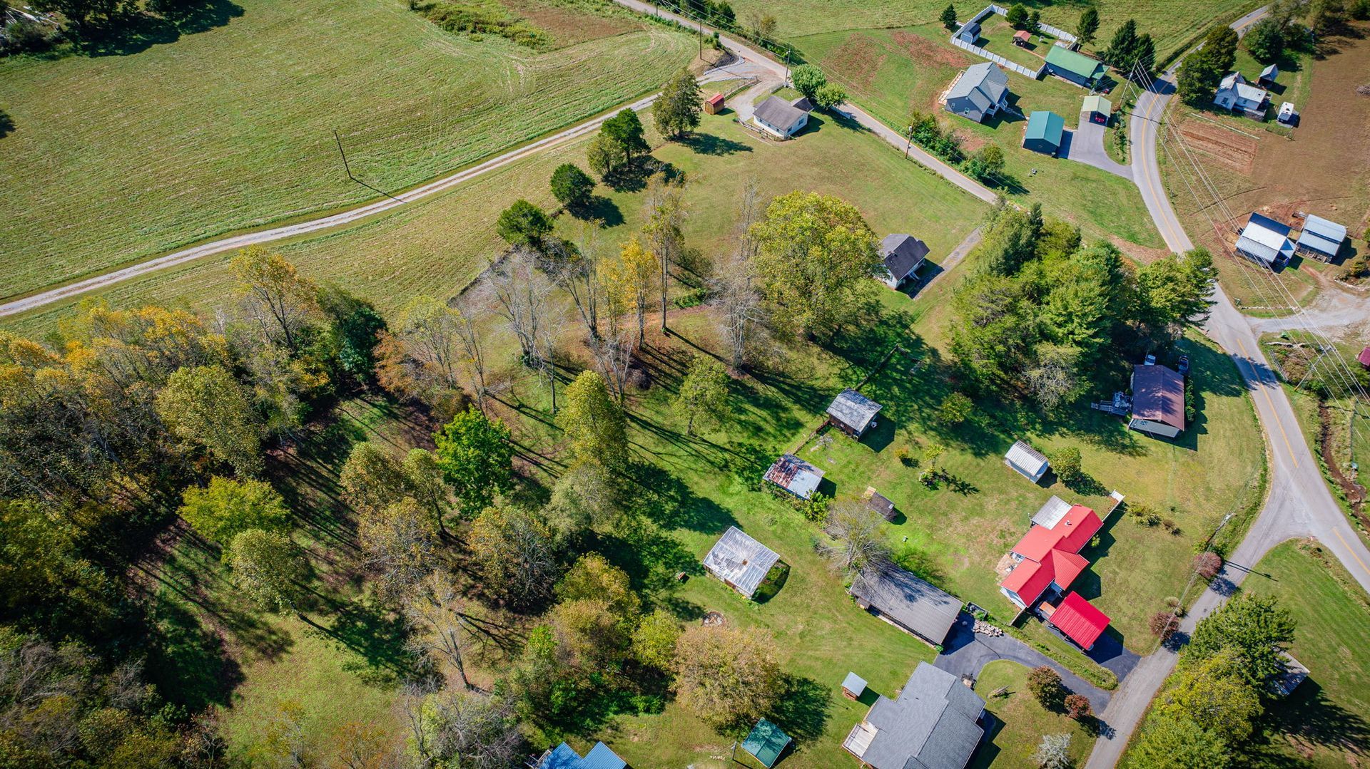 Aerial view of a rural campsite with tents, RVs, and parked vehicles beside fields and trees