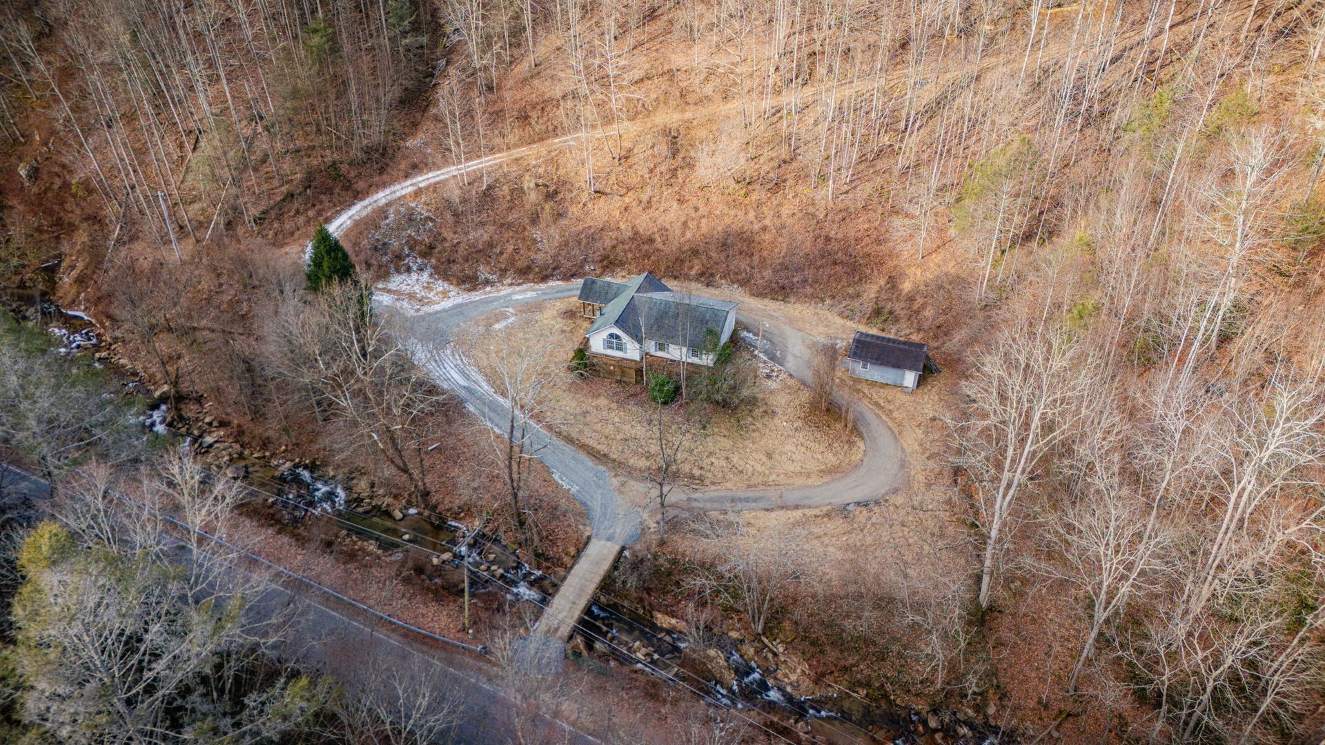 Aerial view of a house and small shed in a wooded area with winding paths.