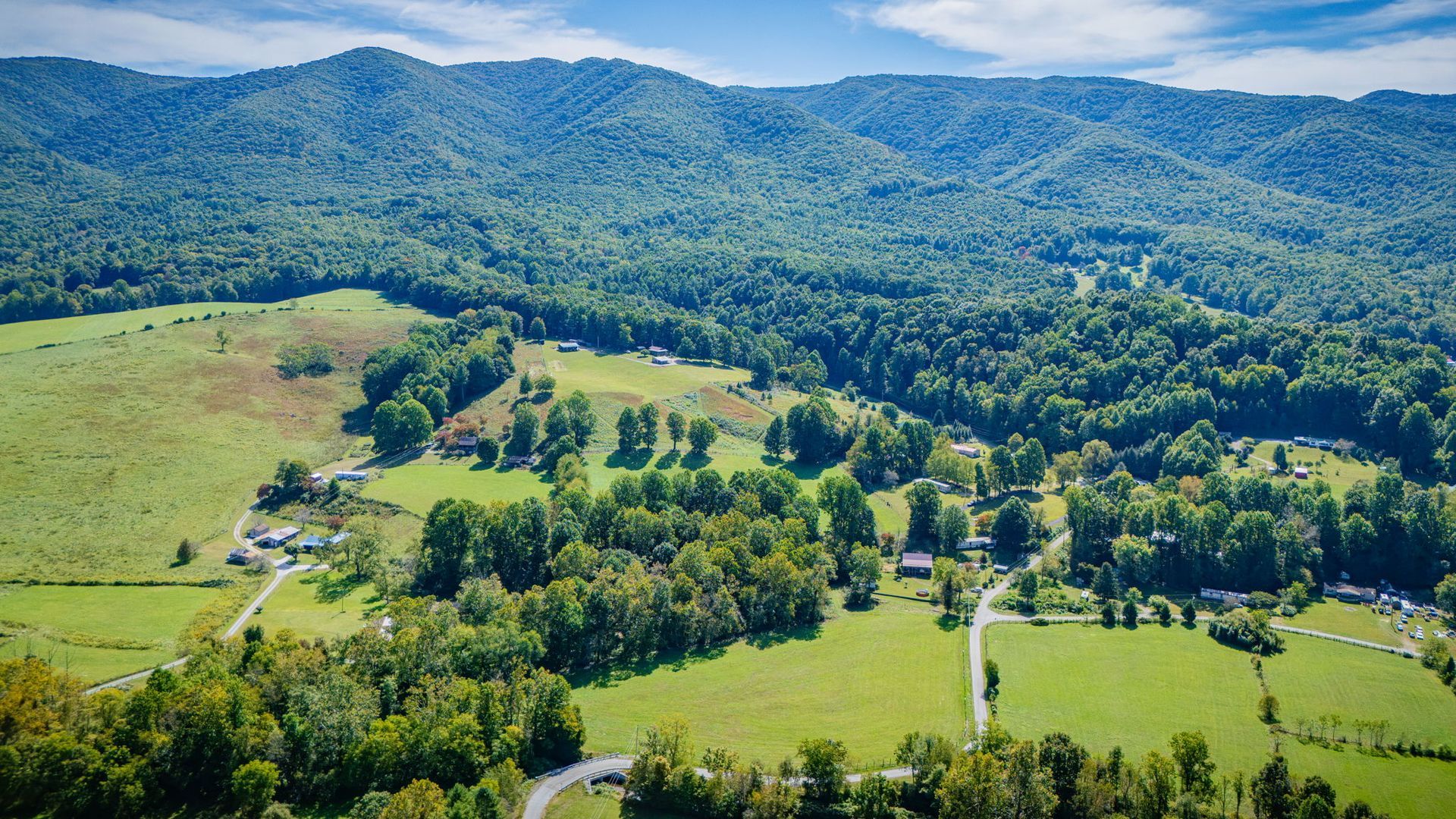 Aerial view of green fields, forest, and rolling mountains under a clear blue sky