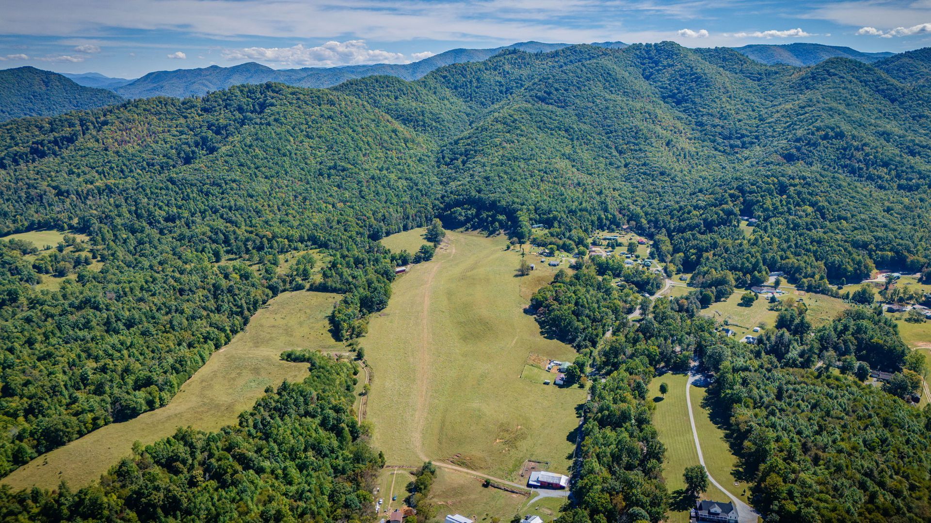 Aerial view of a green valley with mowed fields, forested hills, and a few scattered buildings