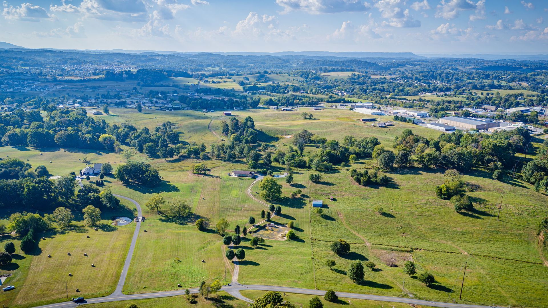 Aerial view of a green parkland with scattered trees, paths, and a city skyline in the distance