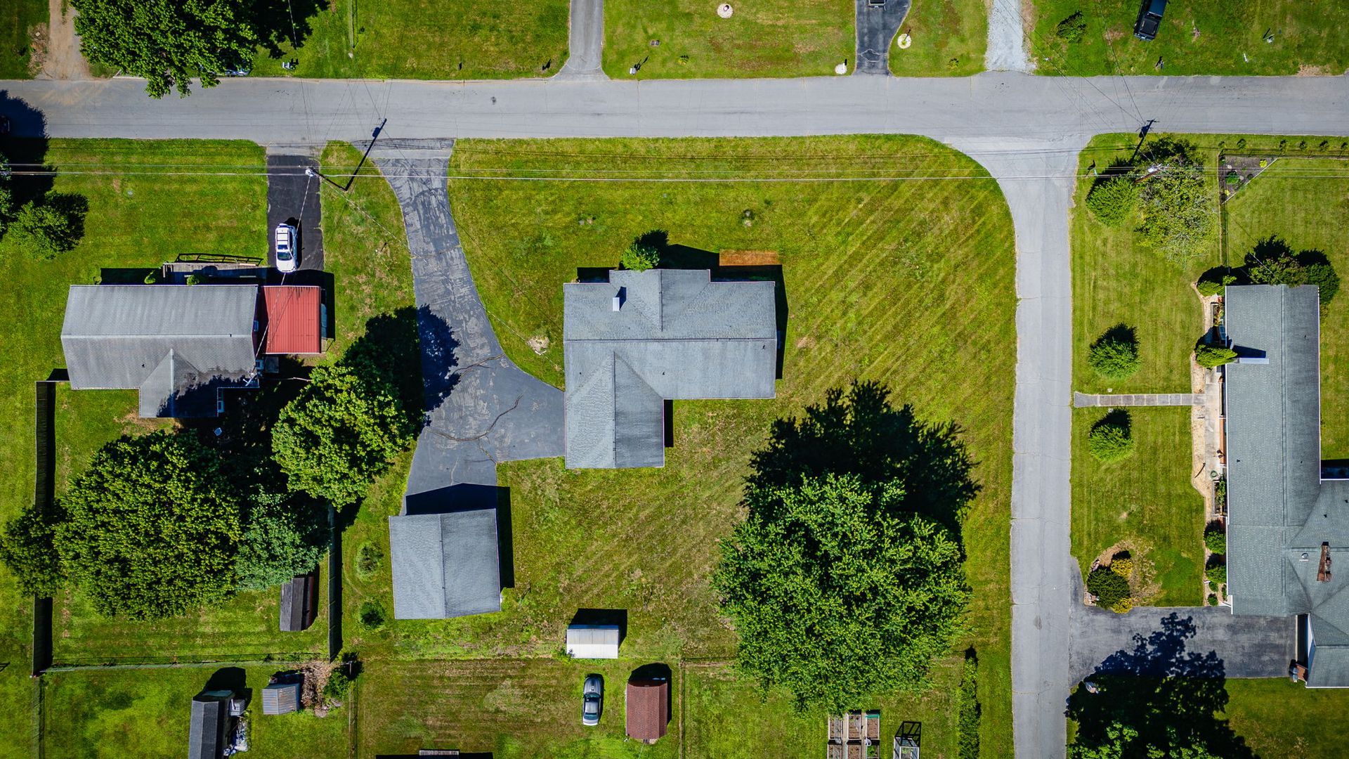Aerial view of suburban homes with green lawns, trees, and a street grid.