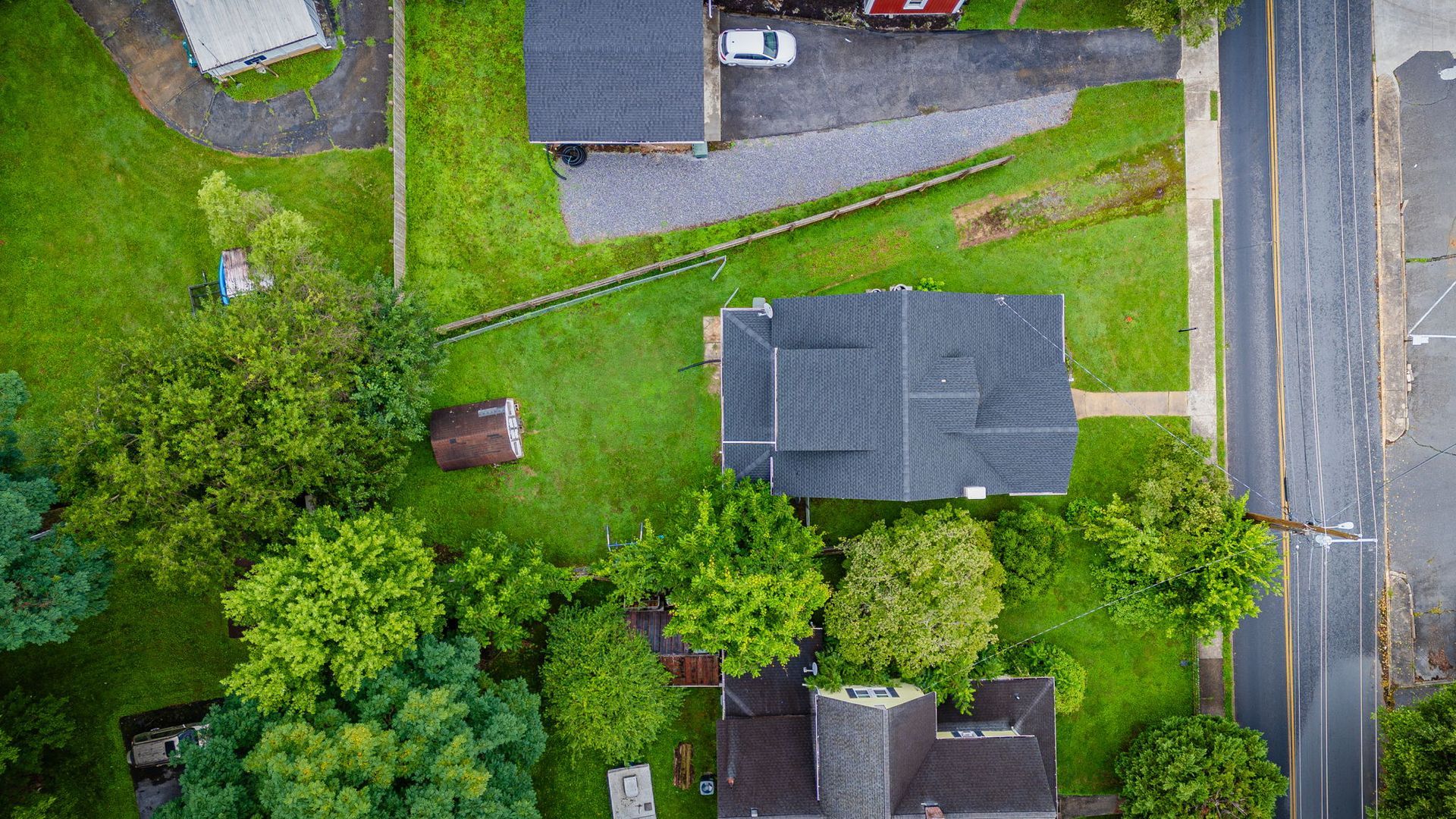 Aerial view of suburban houses, green lawns, trees, and a road along the right side