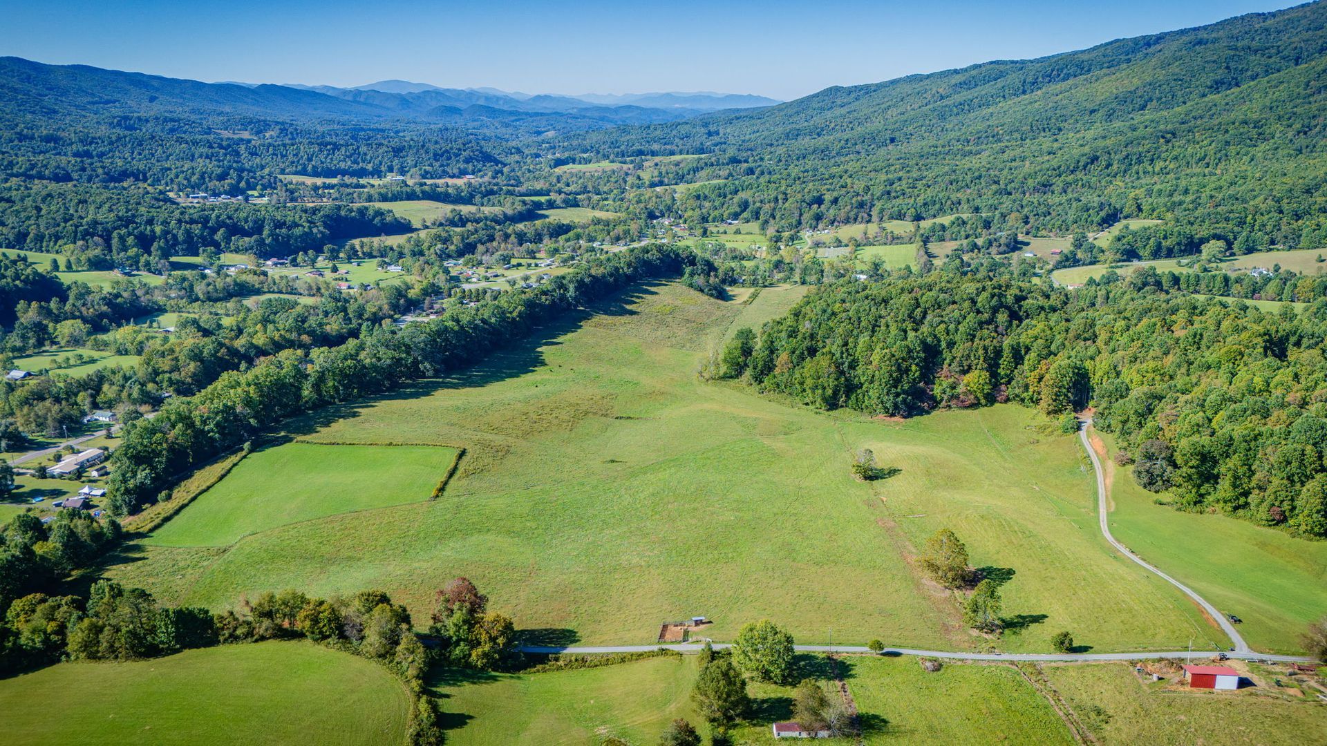 Aerial view of a green valley with fields, trees, rolling hills, and a winding road under clear blue sky