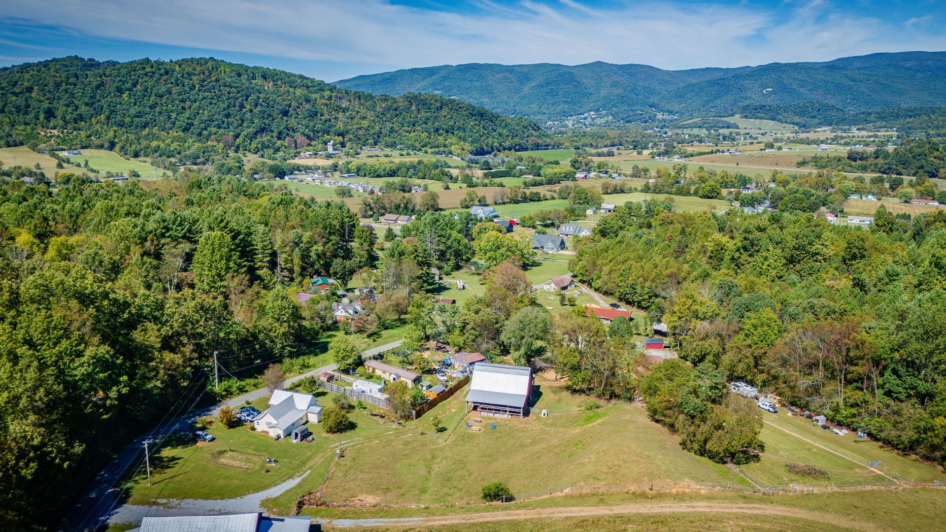 Wide aerial view of a green rural valley with scattered houses, fields, and tree-covered hills