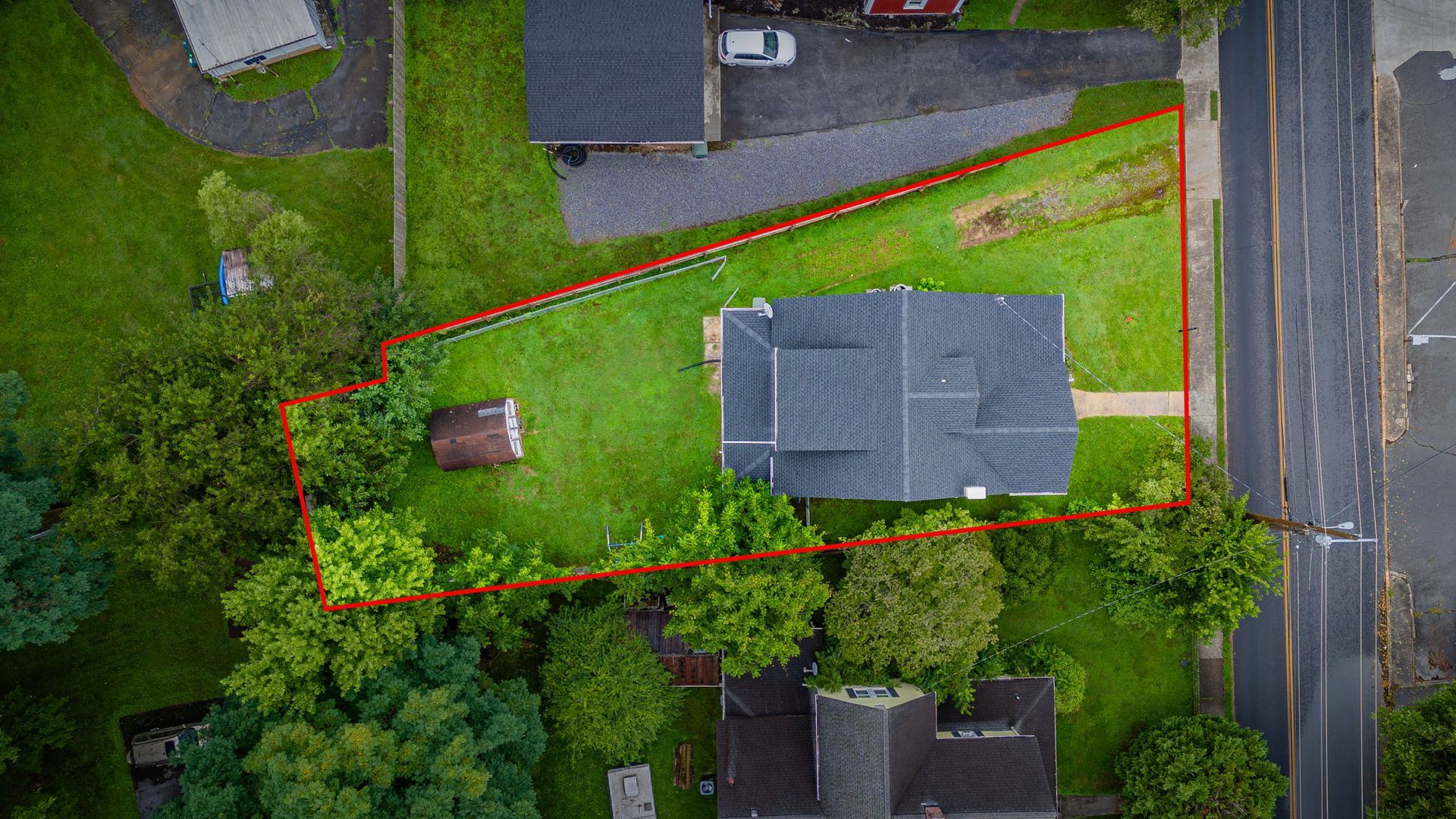 Aerial view of a house and yard outlined in red beside a road, with trees and grass around it