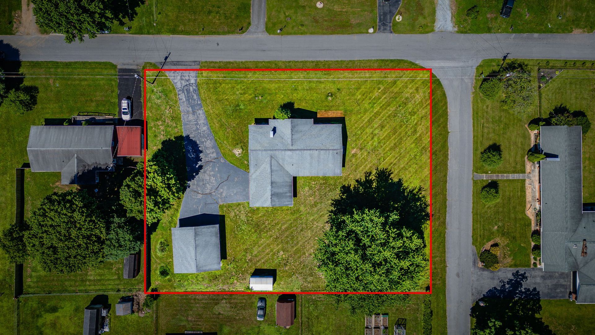 Aerial view of a suburban house with red boundary lines, surrounded by green lawns and nearby roads.