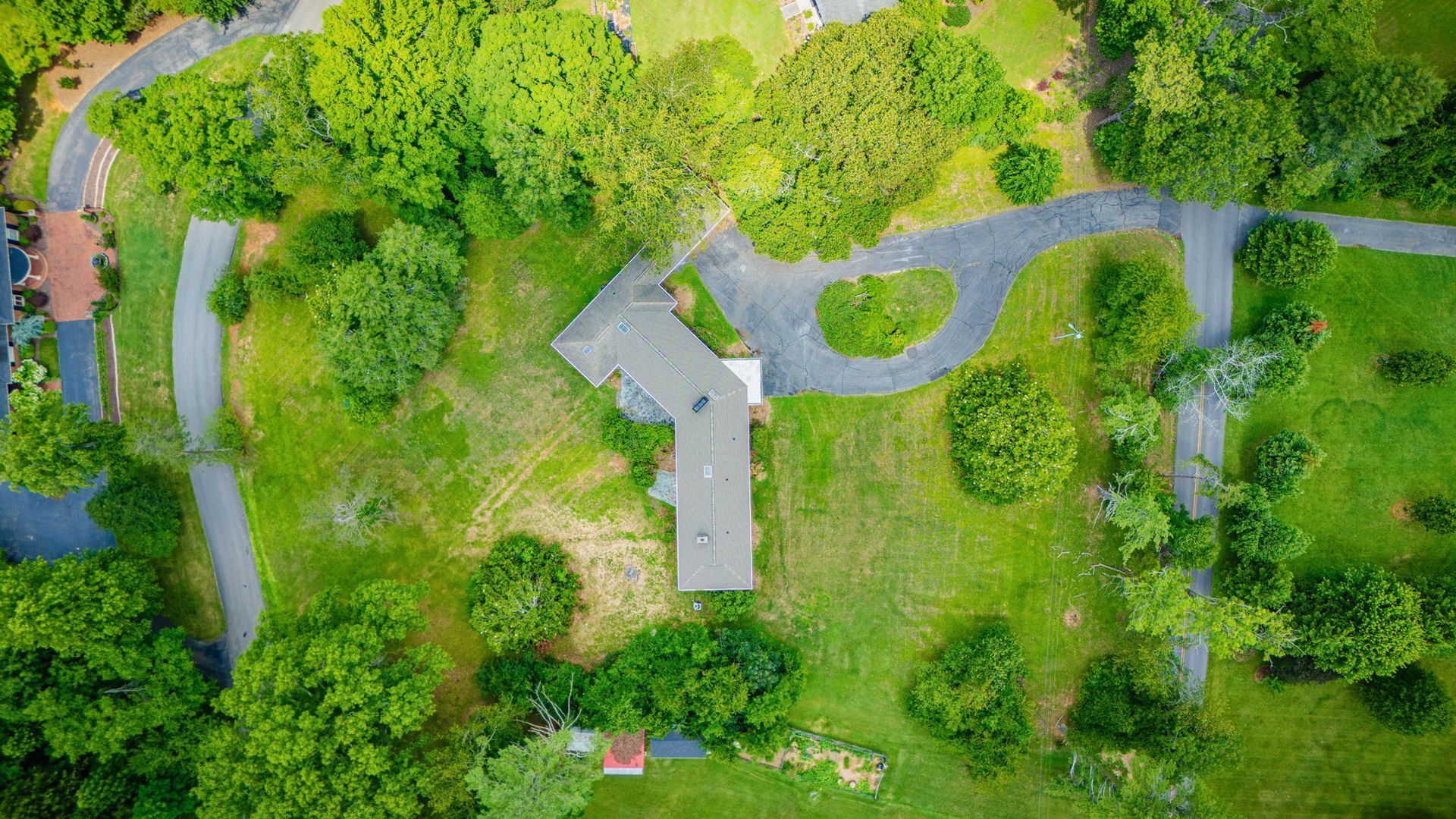Aerial view of a house with a curved driveway, surrounded by dense green trees and lawn.