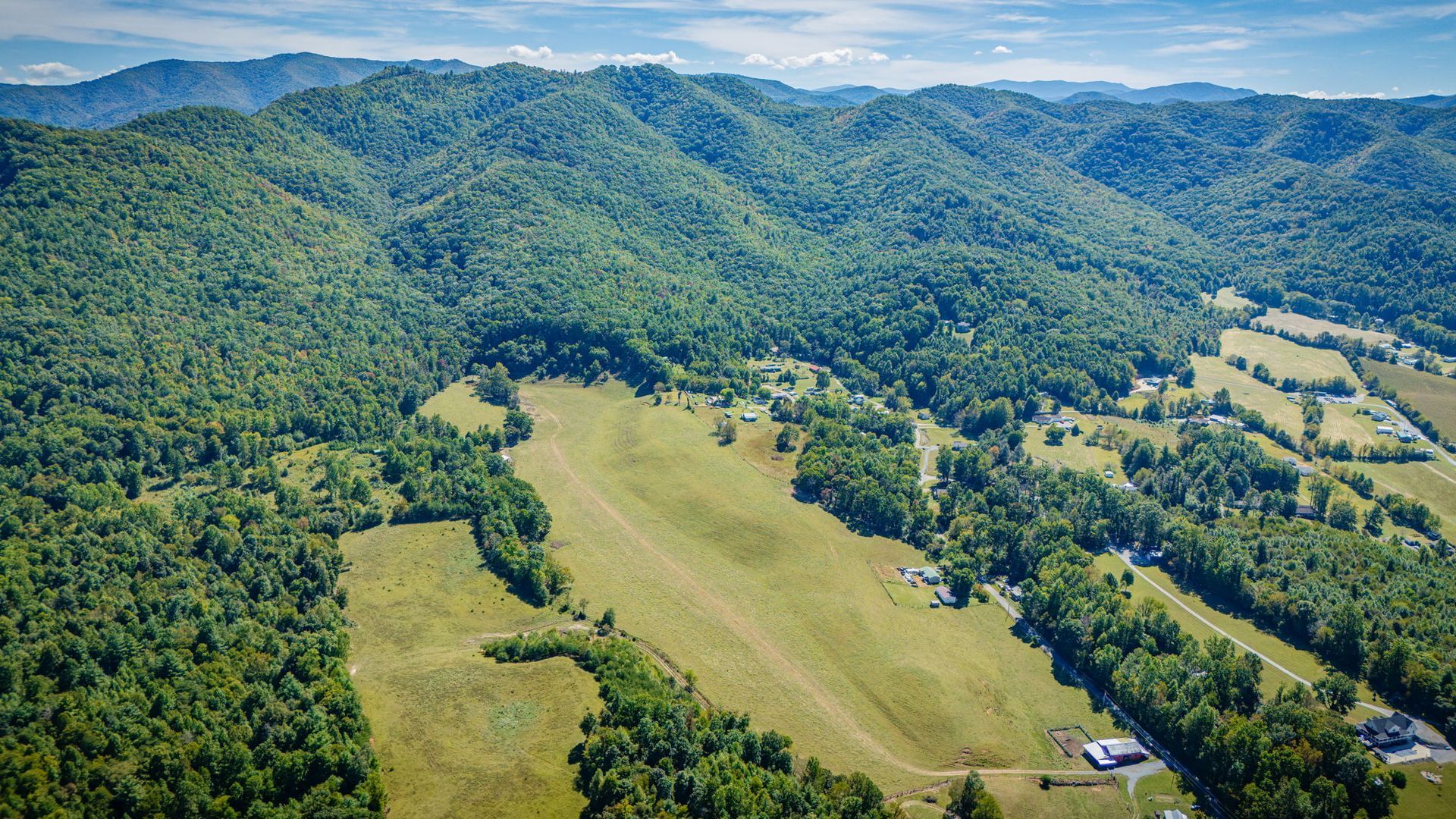 Aerial view of a green forested valley with open fields and distant mountains under a clear blue sky