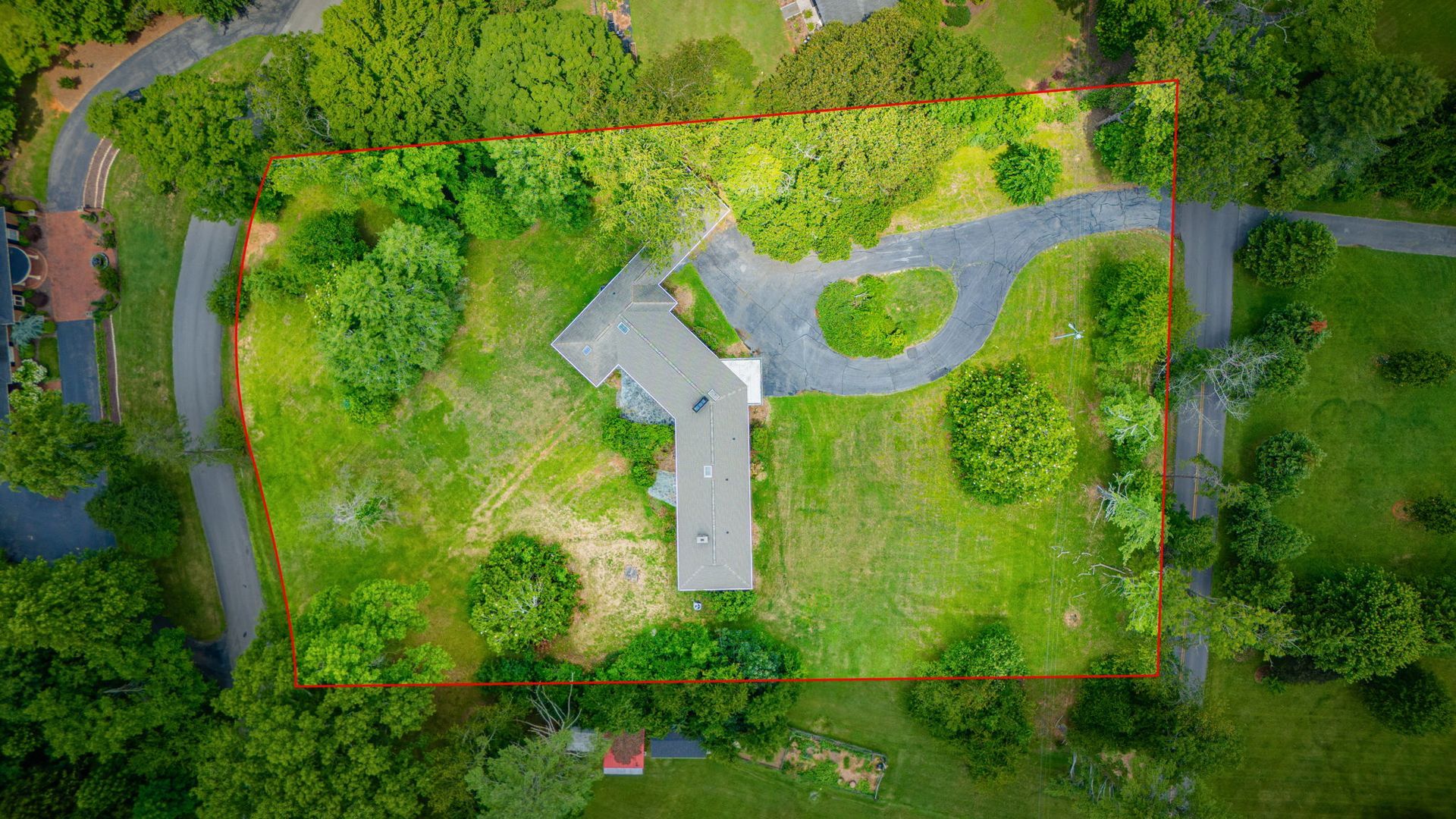 Aerial view of a house with a driveway, surrounded by lush green trees and lawn.