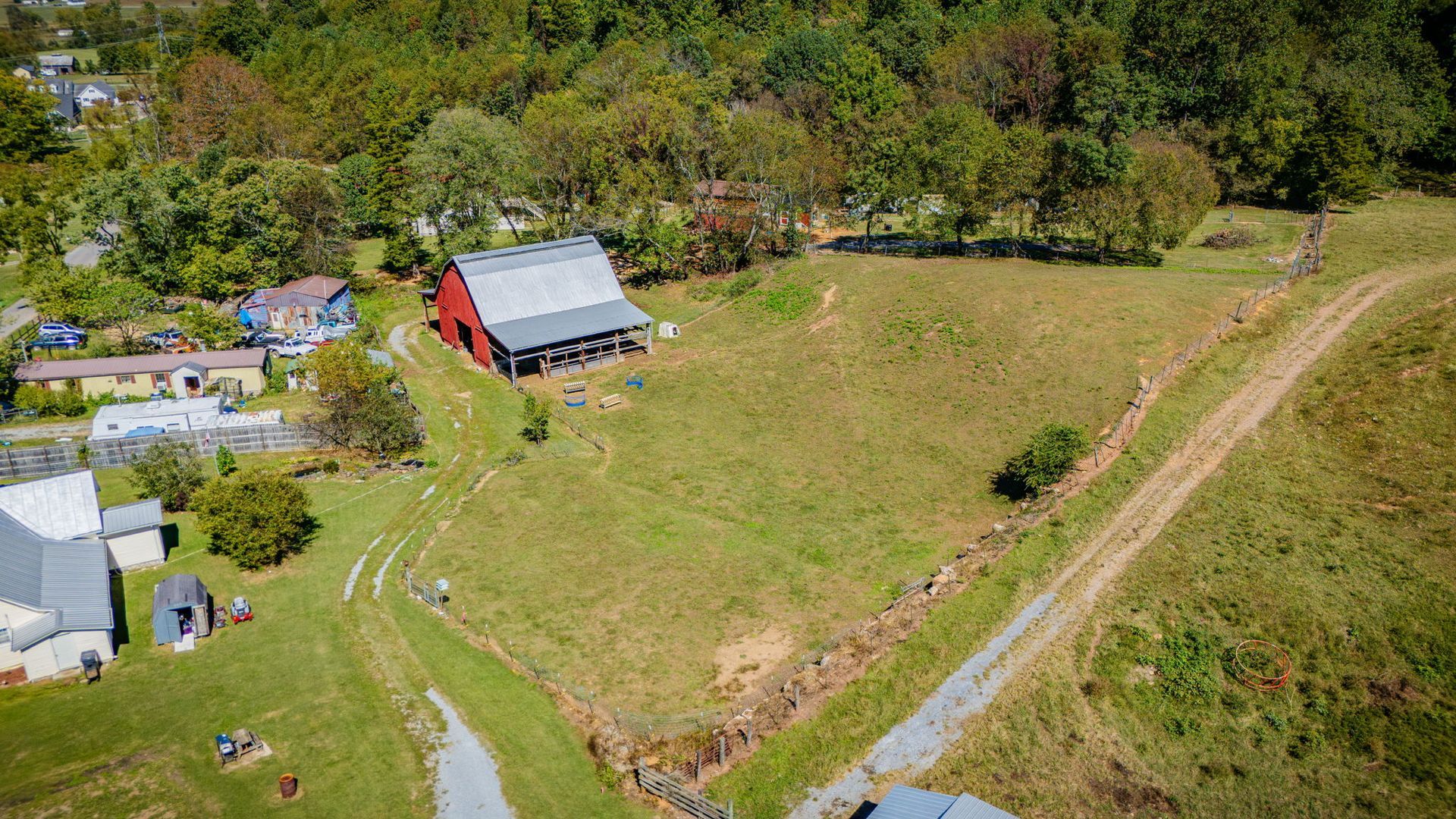 Aerial view of a rural farm with barns, open grassy fields, and trees along a dirt road.