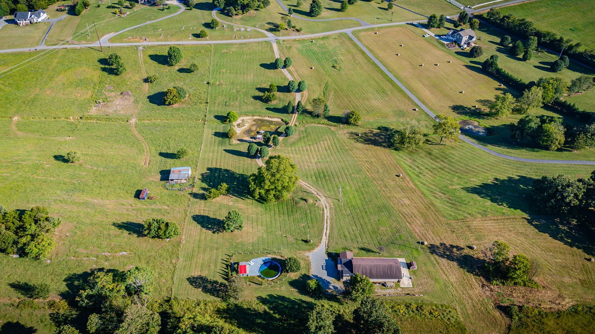 Aerial view of a rural farm with scattered houses, dirt roads, and green fields under sunny skies
