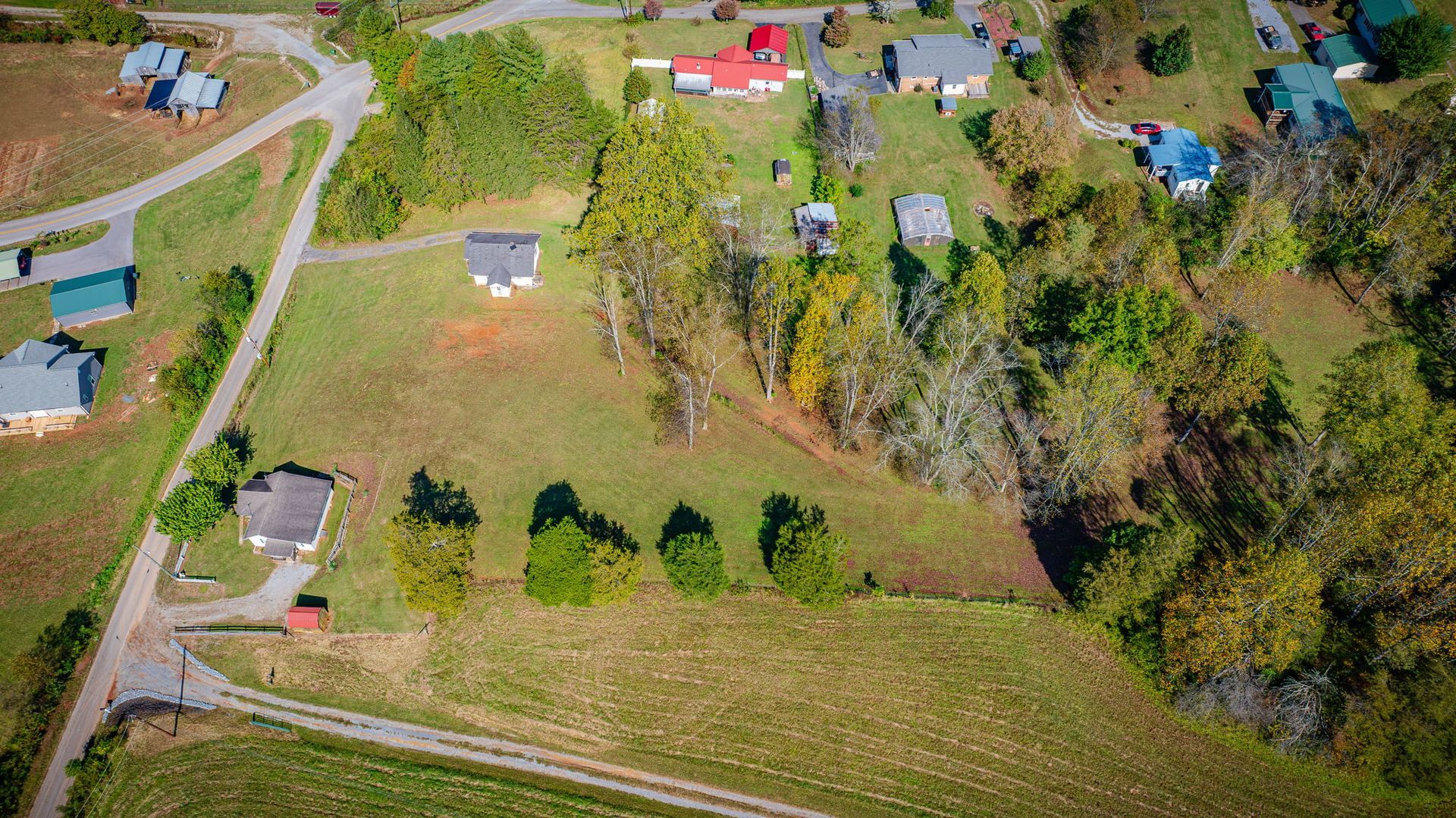 Aerial view of rural homes, fields, and trees along winding roads in autumn colors