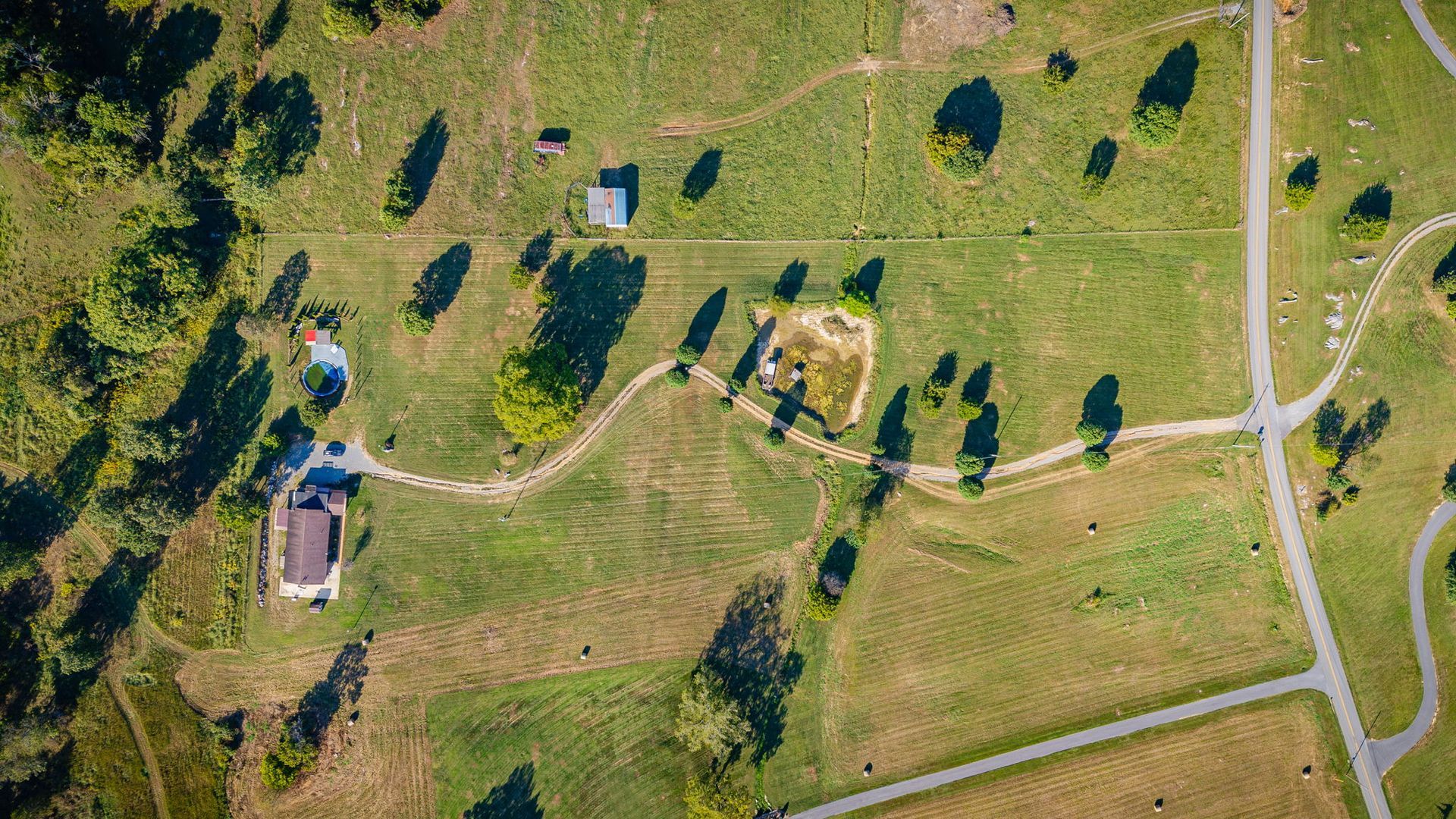 Aerial view of a green park with winding paths, scattered trees, and a small building near the lower left.