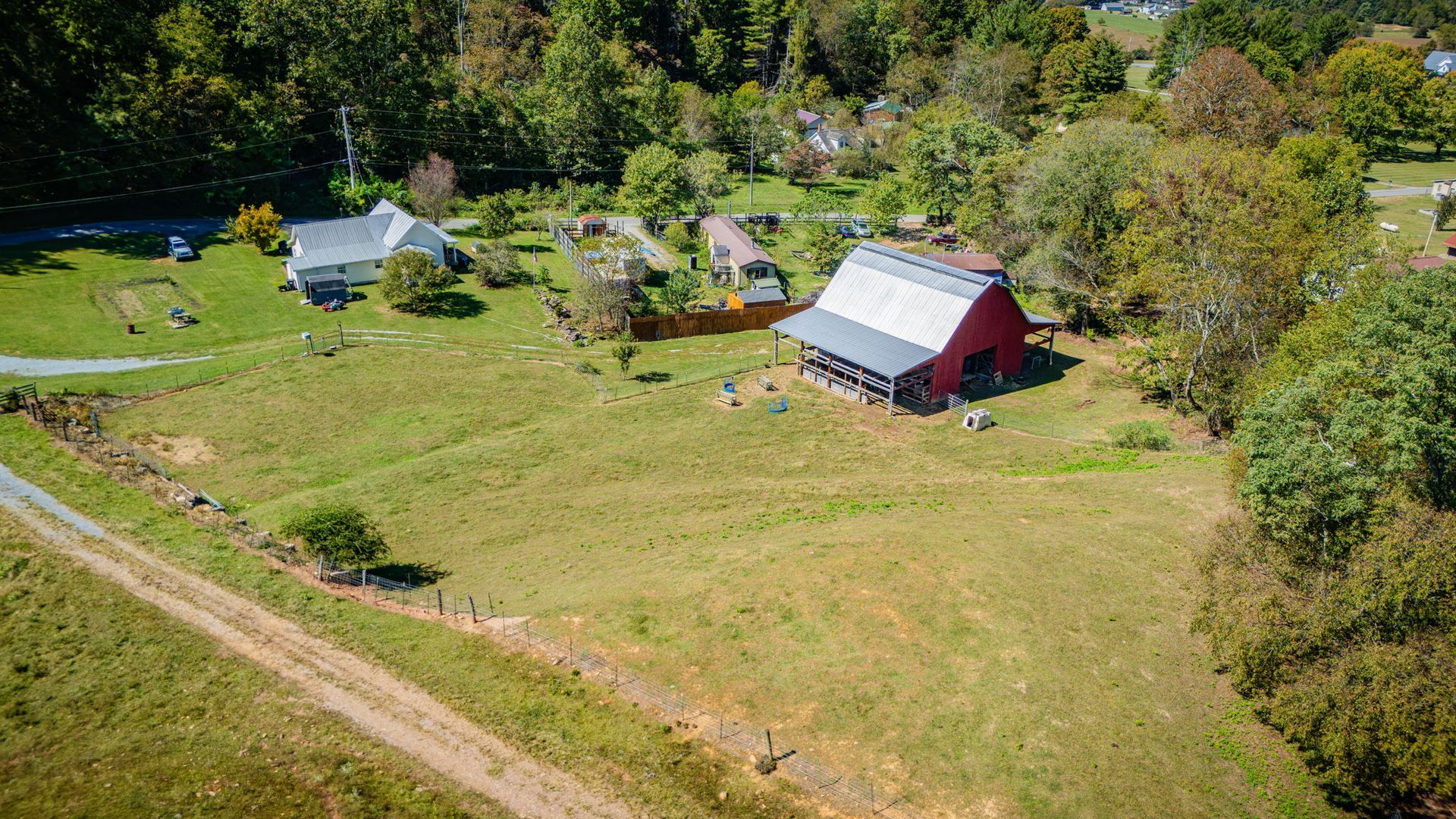 Aerial view of a farm with a red barn, white house, and grassy fields surrounded by trees.