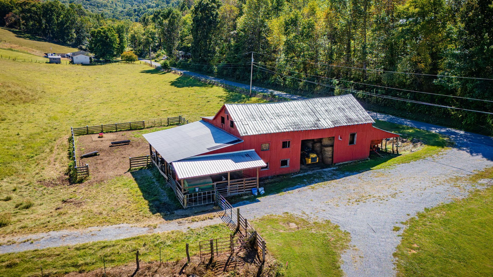 A red farmhouse and gravel driveway beside green fields and trees, viewed from above.