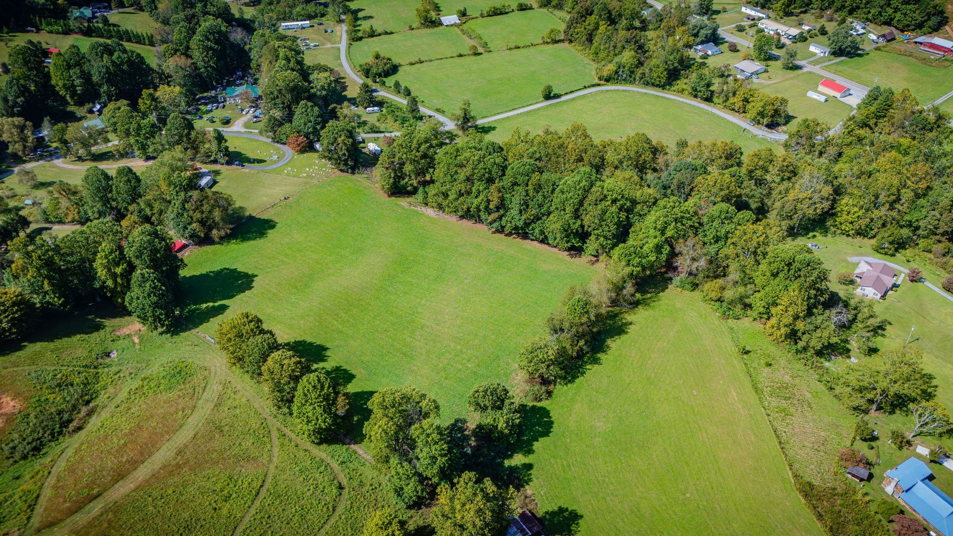 Aerial view of green fields and trees in a rural landscape with scattered houses and roads.