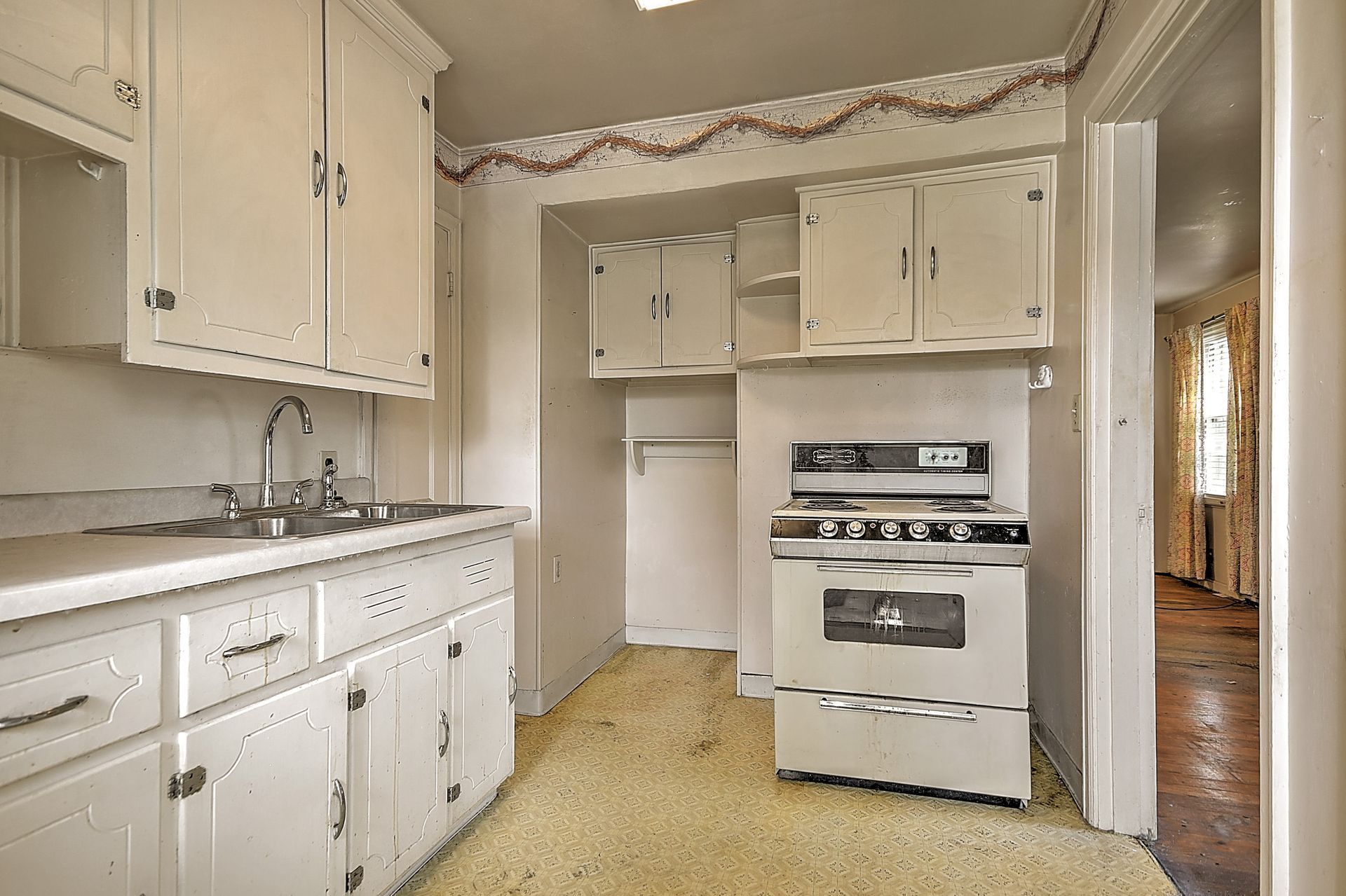Old, worn kitchen with white cabinets, beige walls, and a built-in oven.
