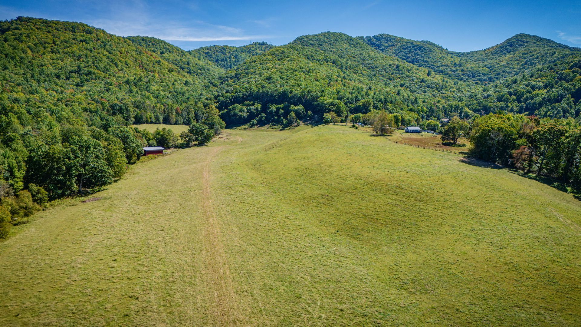 Wide grassy field surrounded by dense green mountains under a clear blue sky