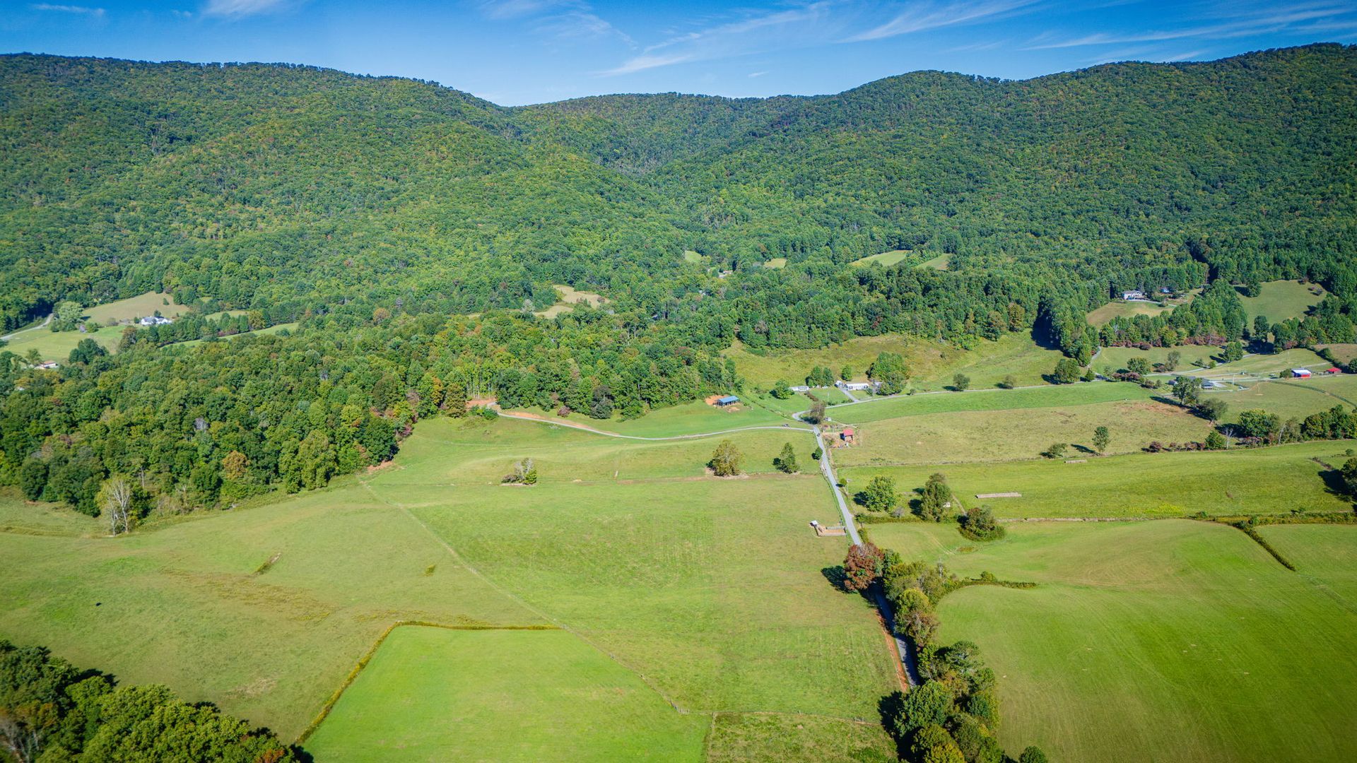 Green valley and farmland at the base of forested mountains under a clear blue sky