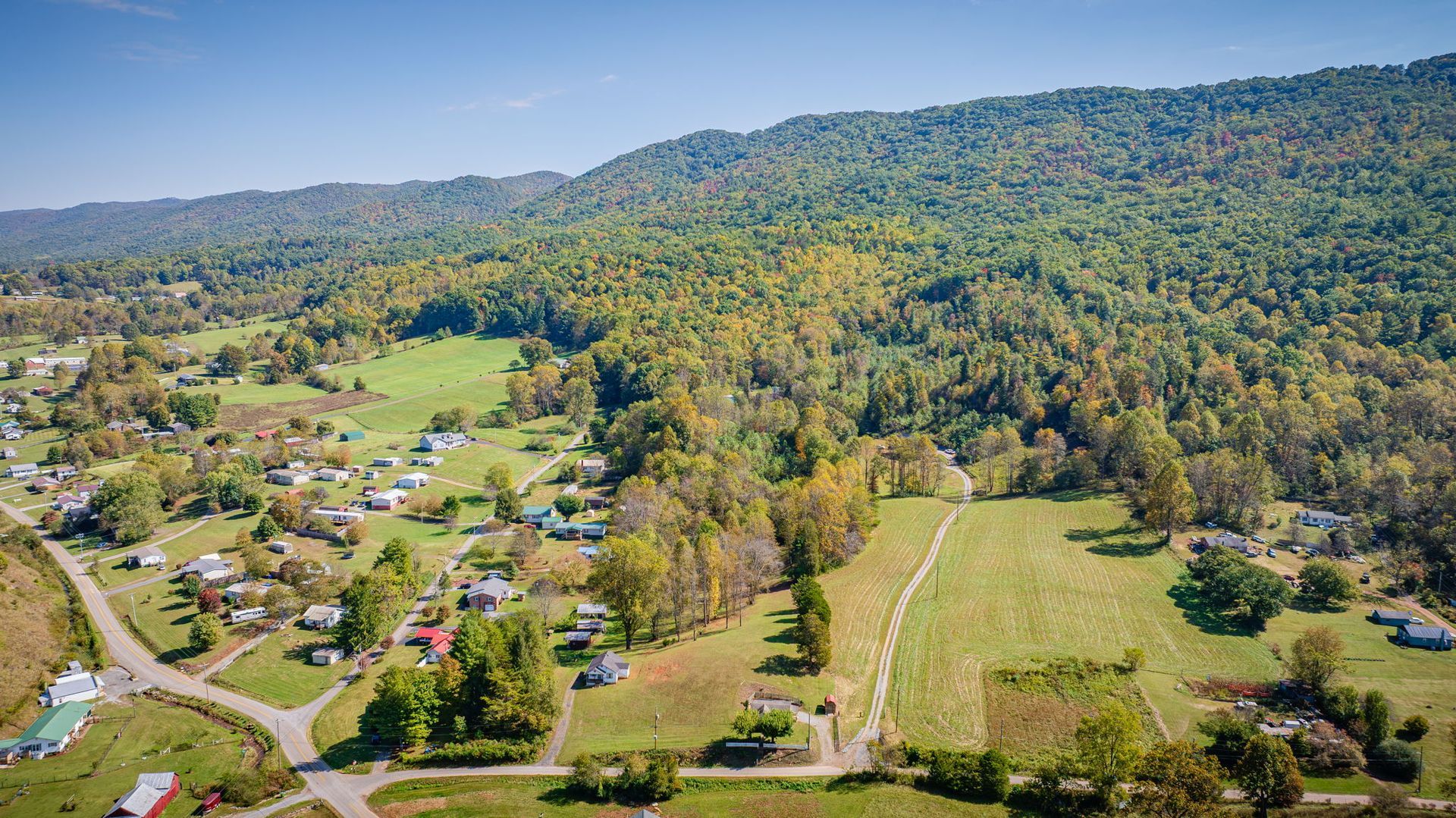 Aerial view of a rural valley with scattered houses, green fields, and forested hills.