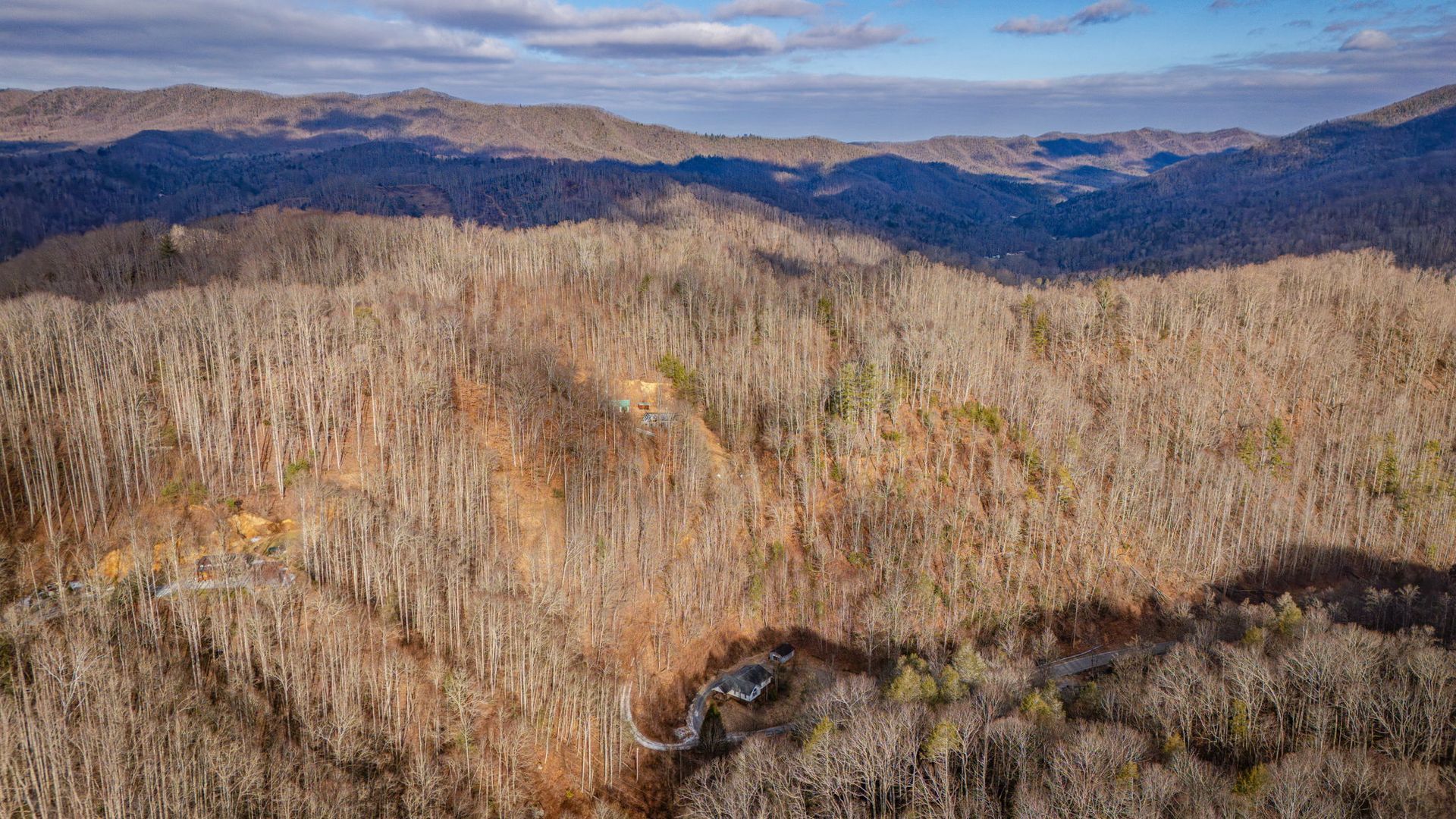 Hillsides covered in leafless trees with shadows from the sun, under a partly cloudy sky.