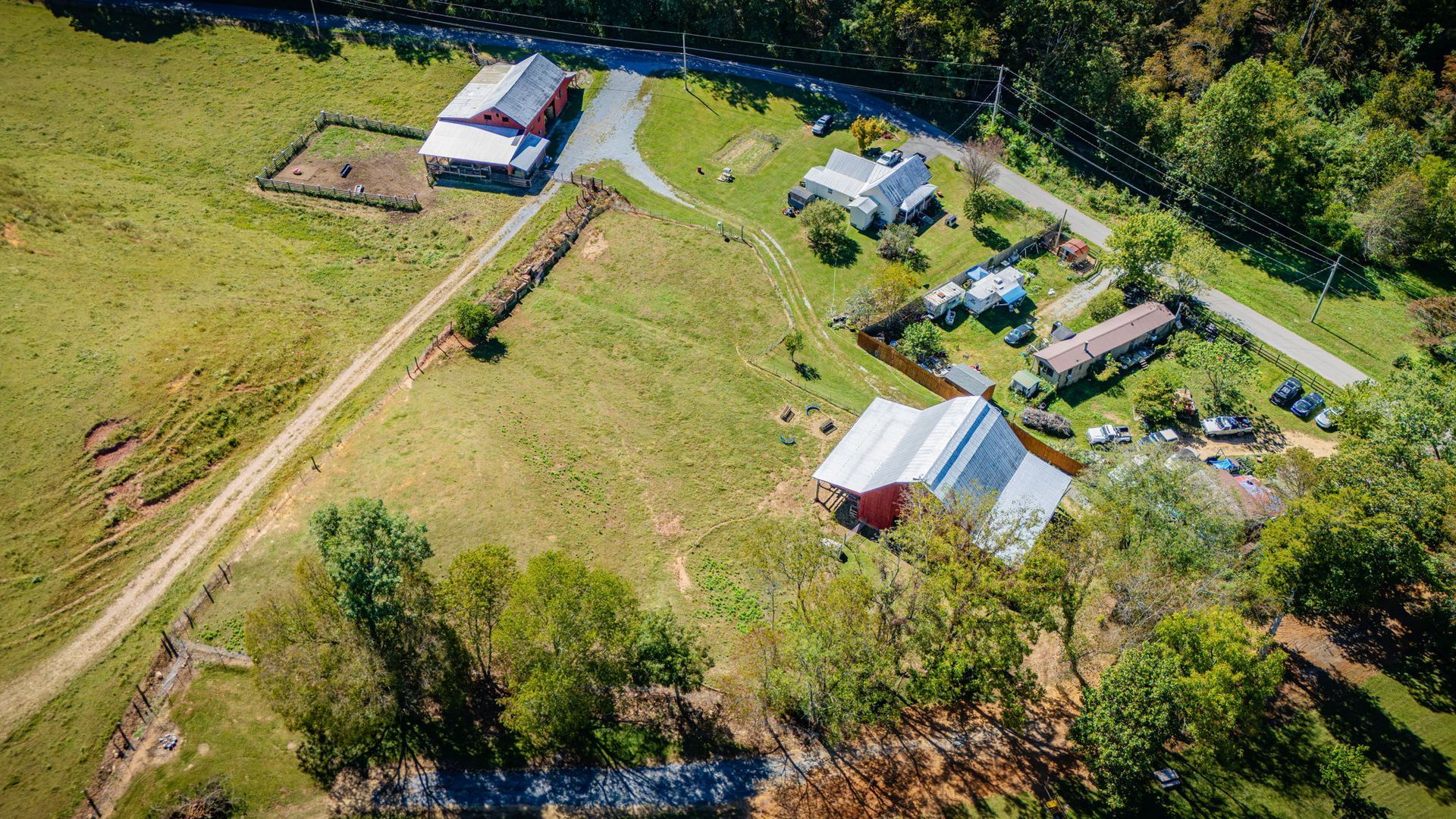 Aerial view of a rural farmstead with barns, houses, dirt roads, and green fields.
