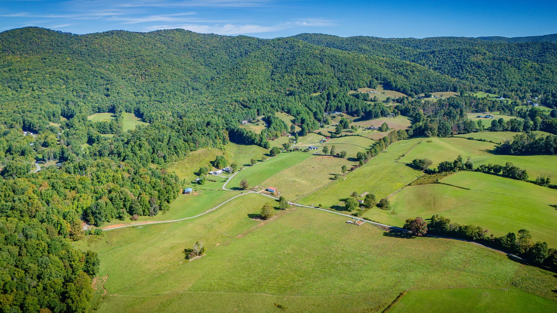 Wide green valley with fields, scattered trees, and forested hills under a clear sky