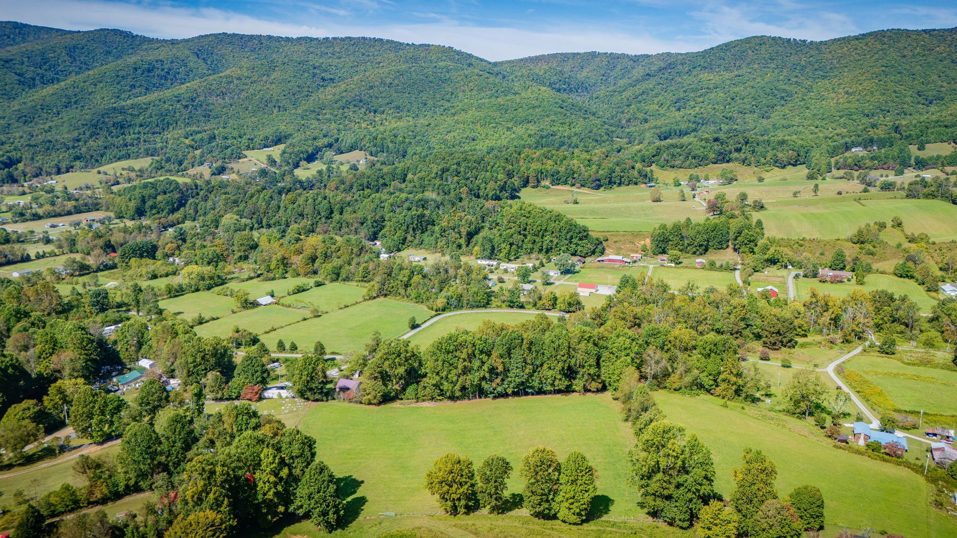 Aerial view of a green rural valley with scattered buildings, fields, trees, and forested hills
