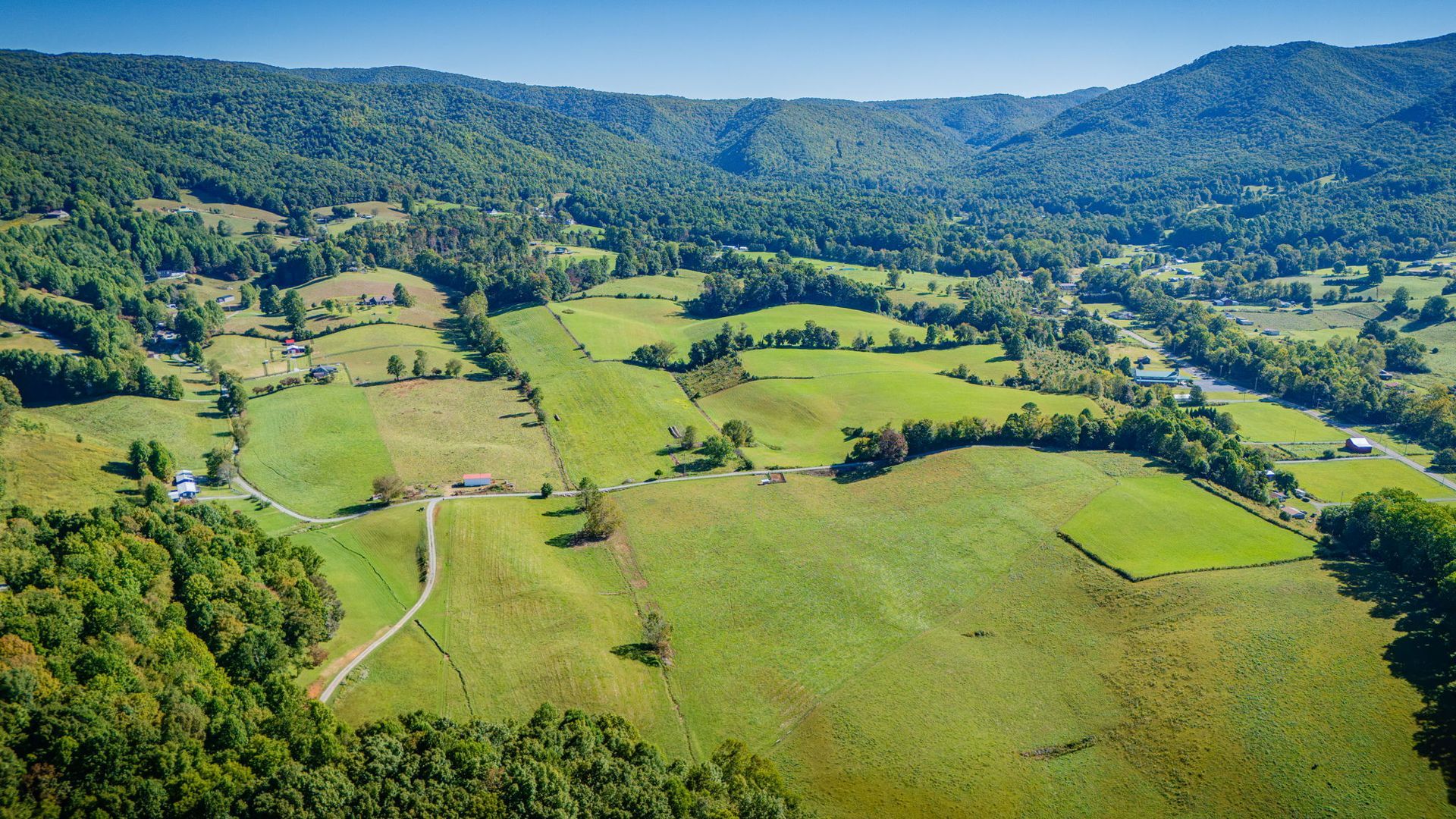 Aerial view of green farmland and forests with rolling hills under a clear blue sky