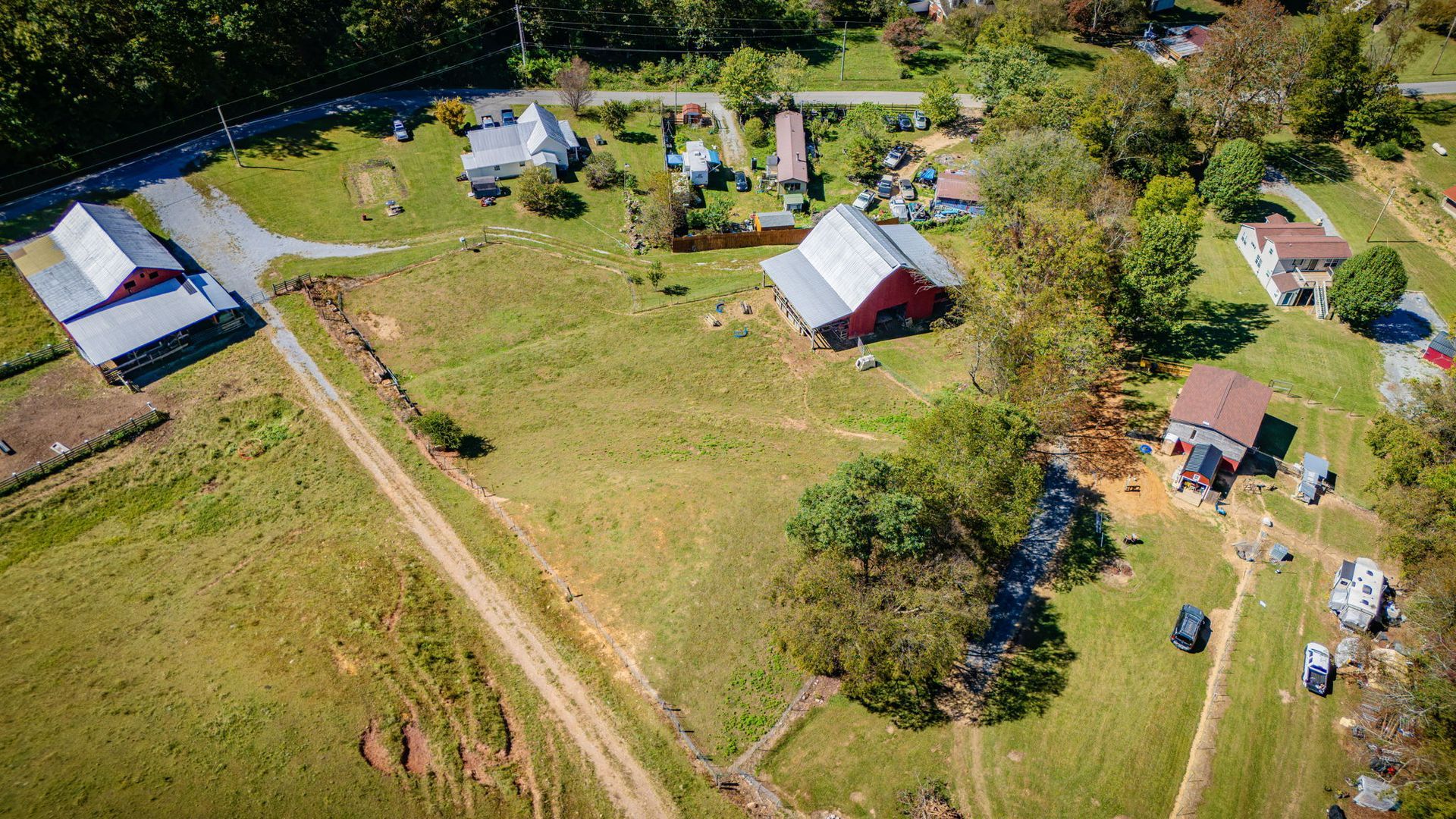 Aerial view of rural homes and outbuildings beside open grassy fields and dirt roads