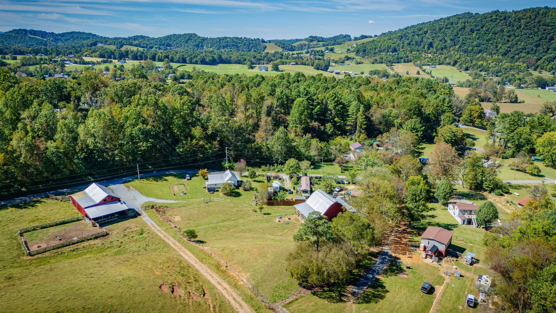 Aerial view of a rural farmstead with barns, houses, fields, and forested hills in the background