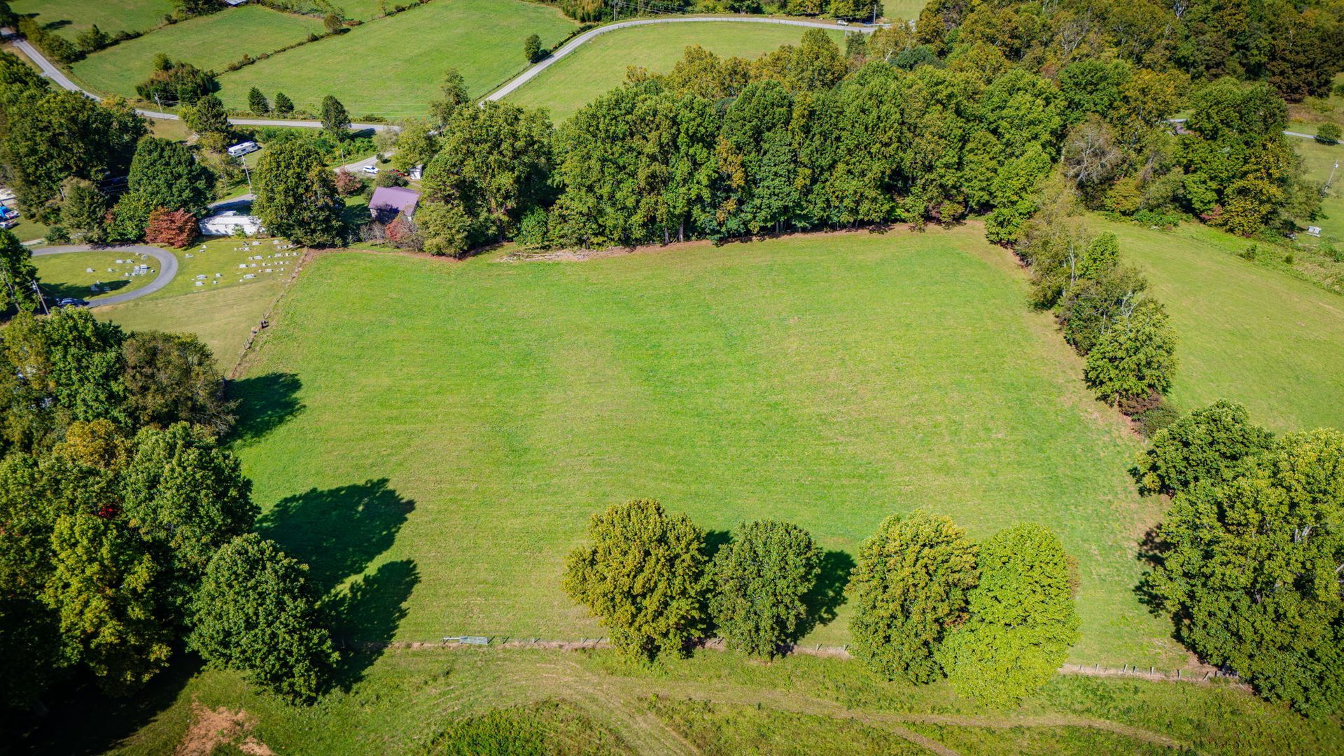 Aerial view of a grassy field surrounded by trees and hedges in a rural landscape.