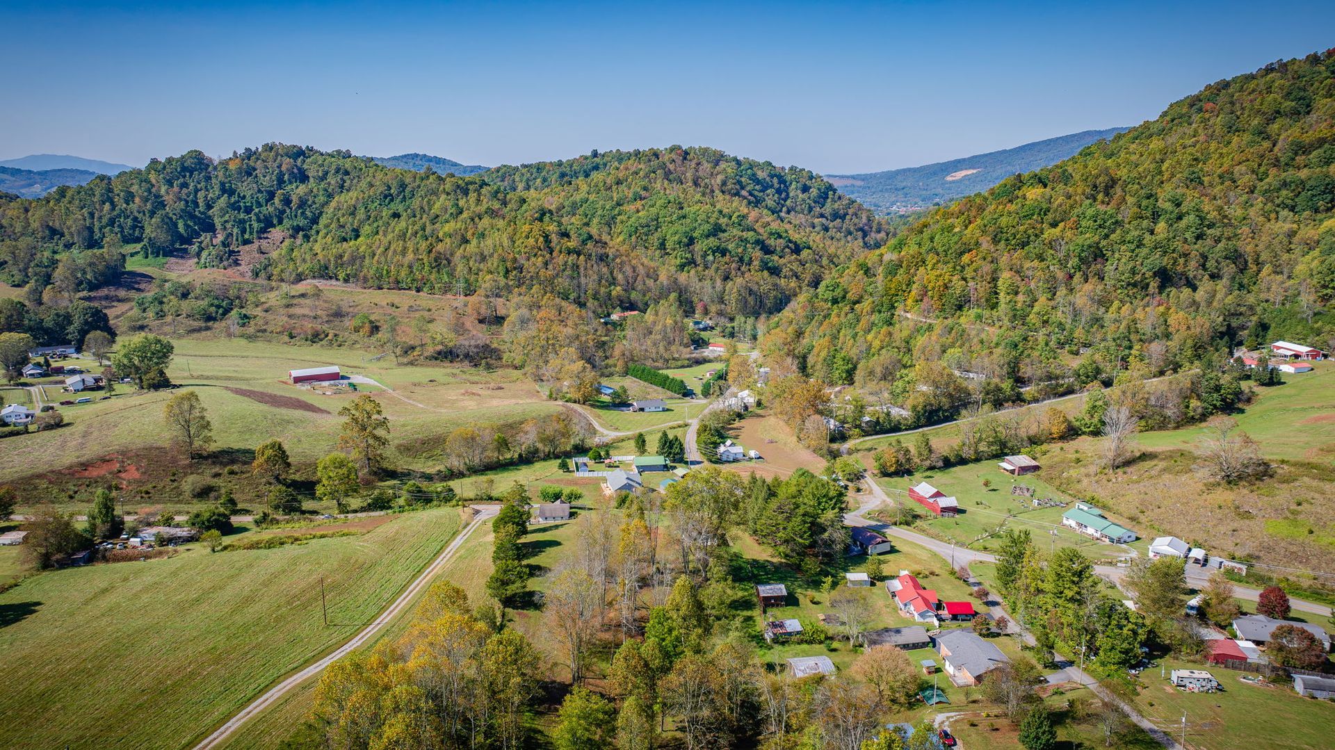 Aerial view of a rural valley with fields, tents, and houses surrounded by forested hills