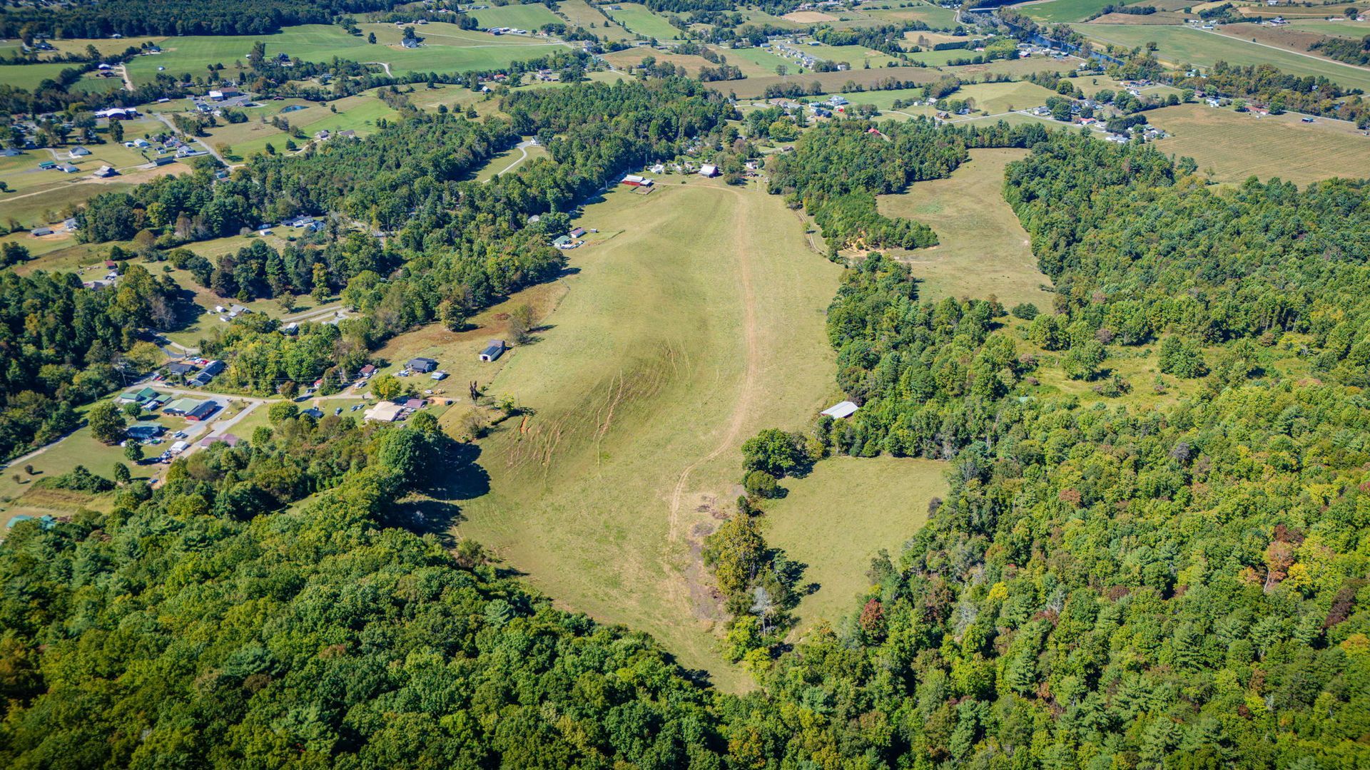 Aerial view of a grassy airstrip surrounded by dense green forest and scattered fields.