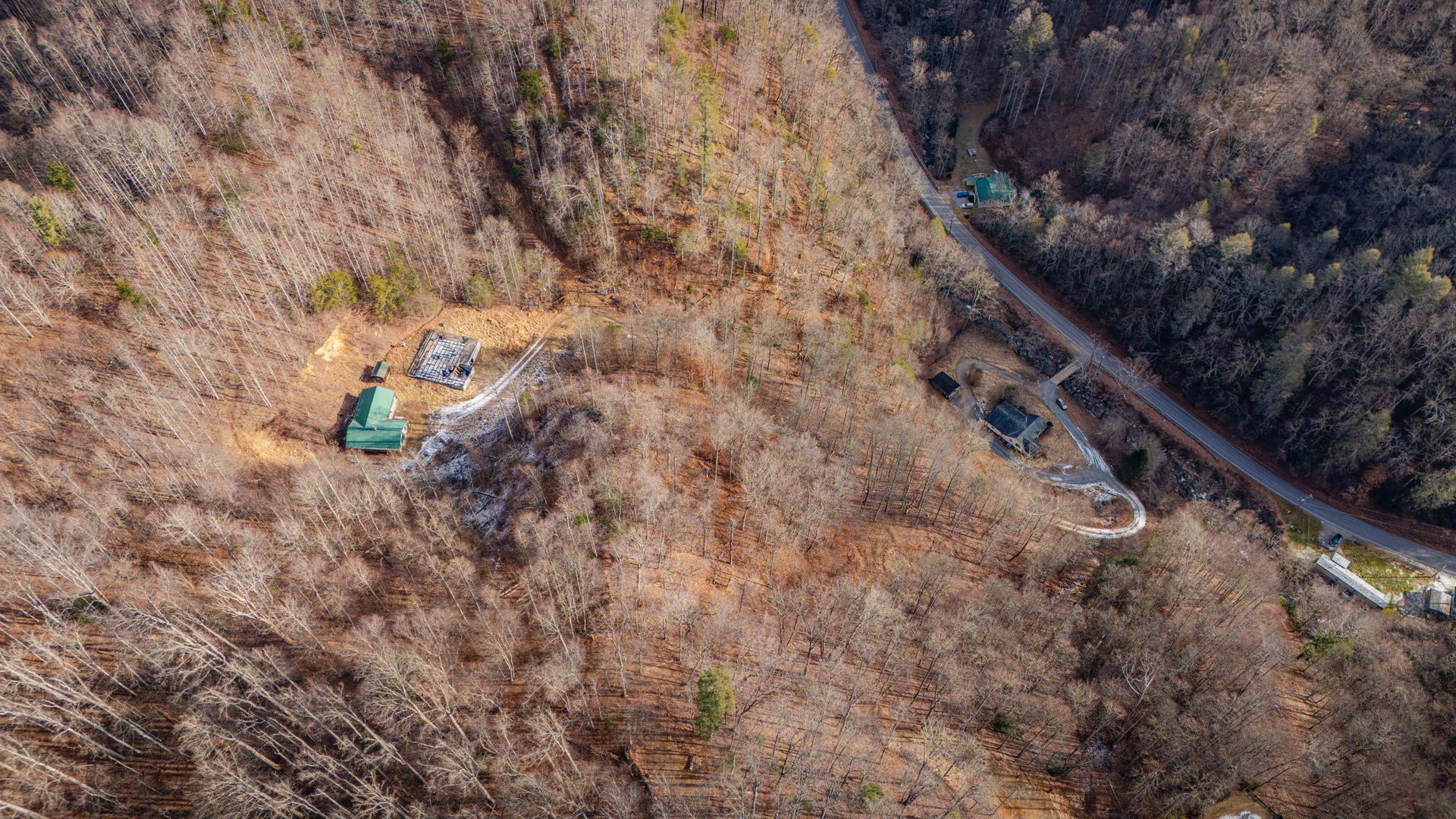Aerial view of houses nestled in a mountain, near a road. Trees are bare, suggesting late autumn or winter.