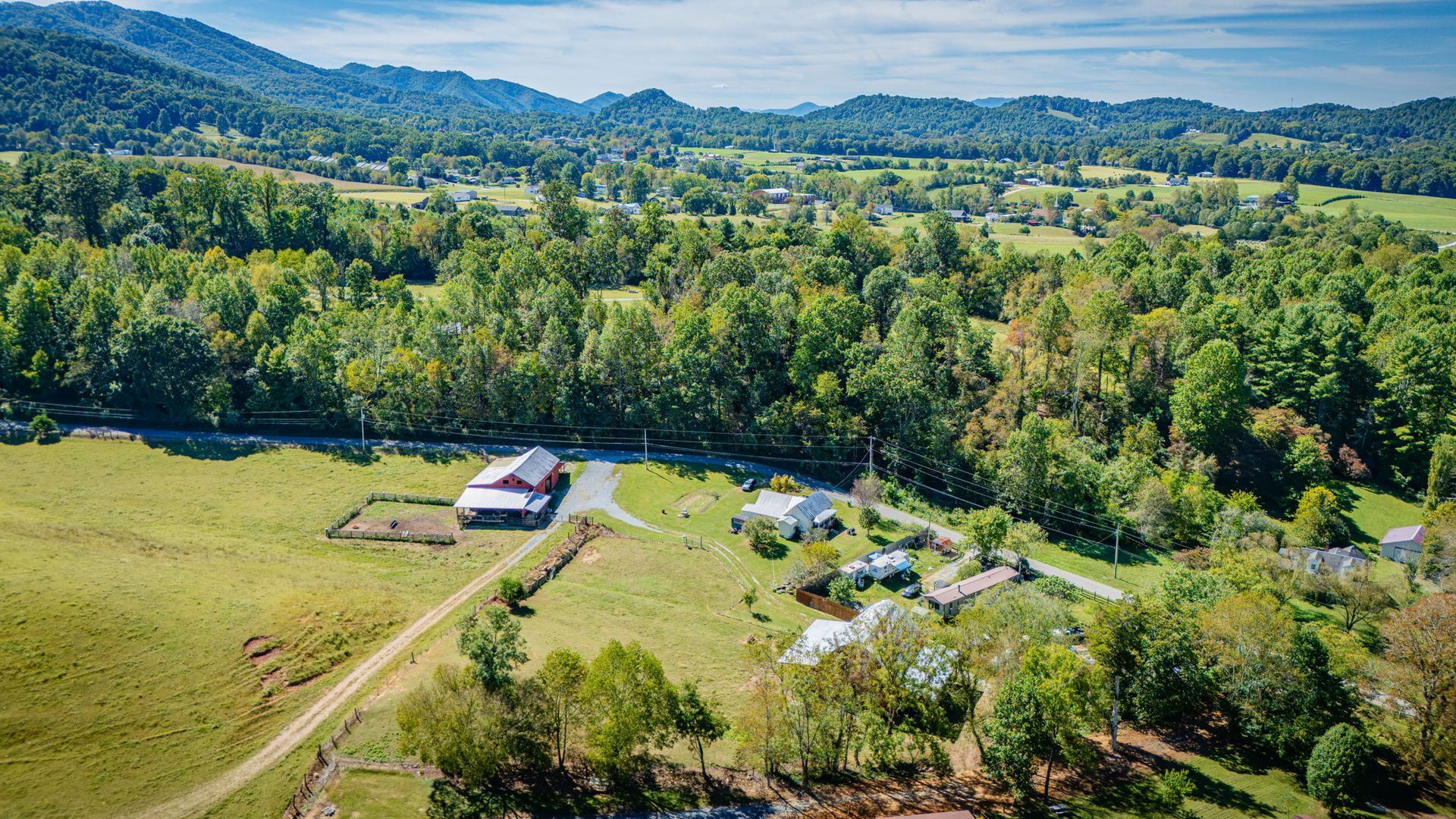 Aerial view of a rural farm with fields, barns, and trees in a green valley surrounded by hills