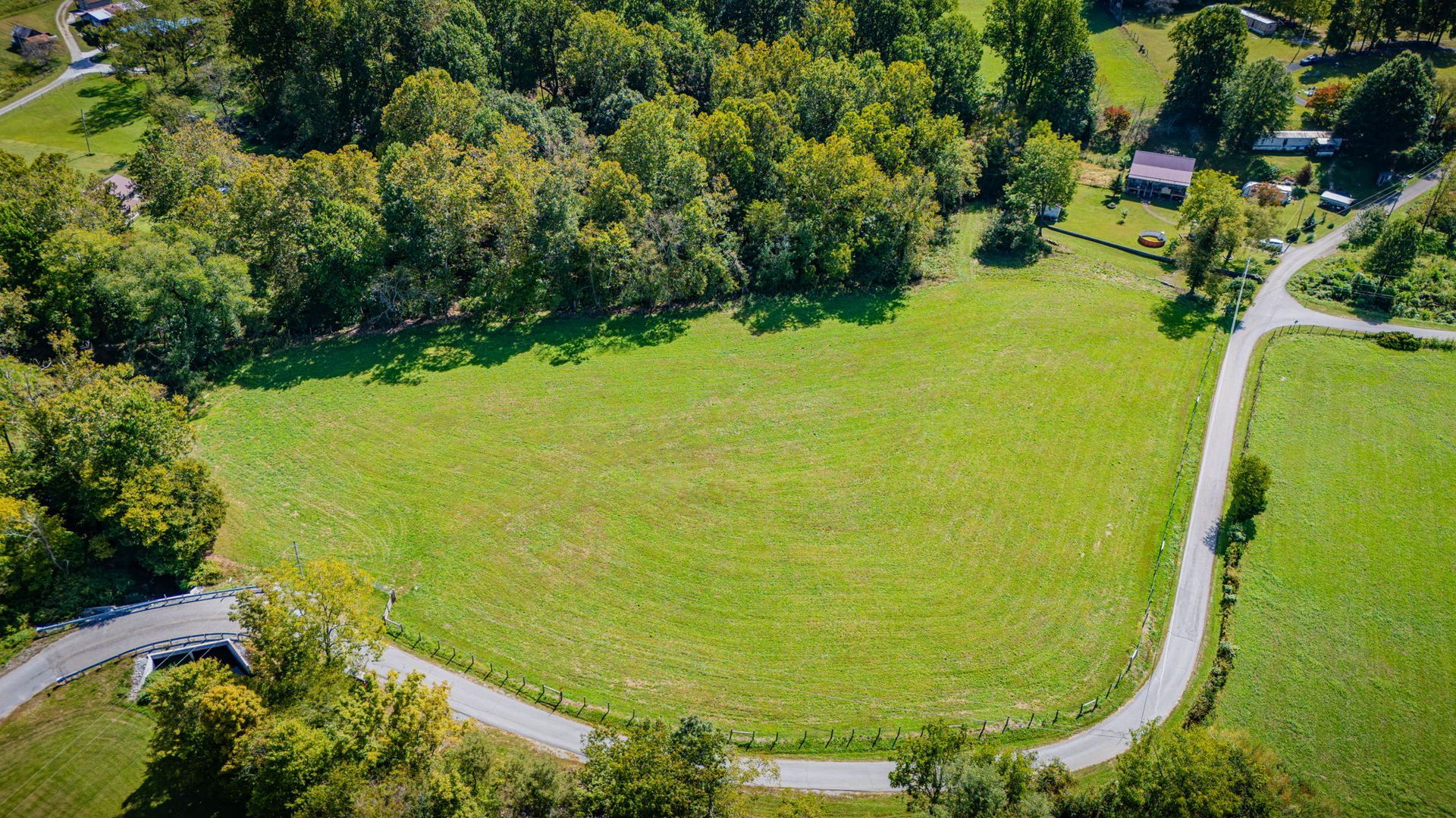 Aerial view of a green field bordered by trees and a winding road.